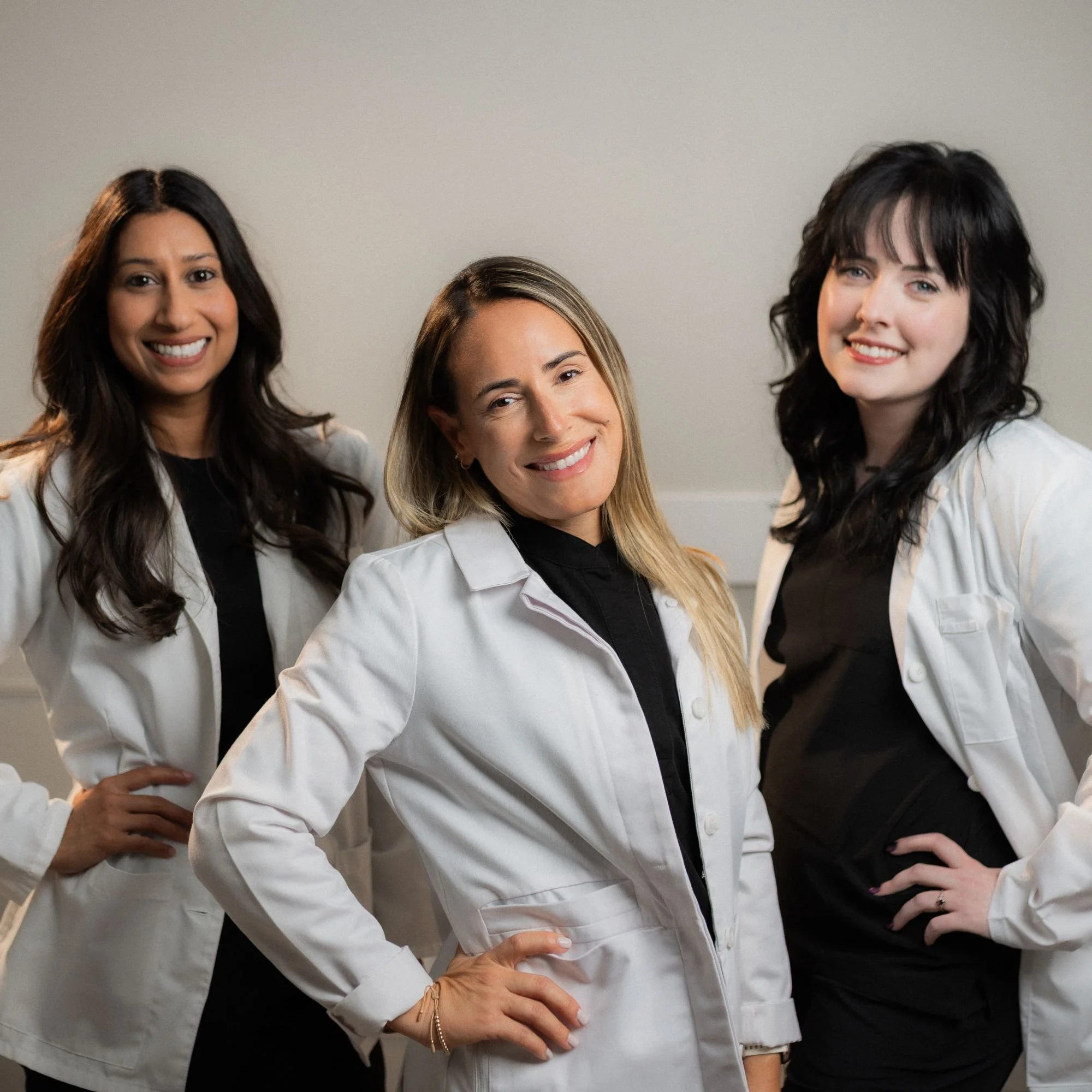 Three women dressed as medical professionals posing together in a clinical setting, all smiling.