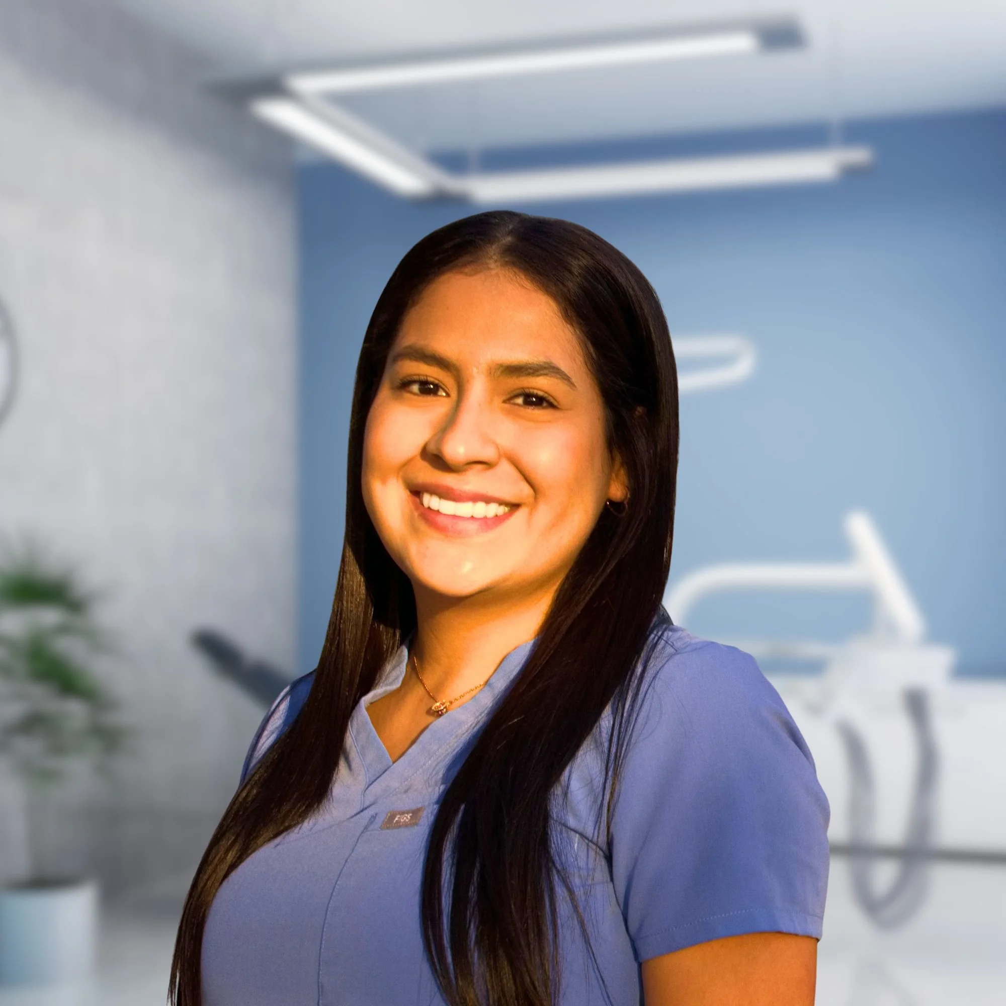 Close-up of a young woman wearing a blue medical uniform, smiling in a clinical or hospital setting.