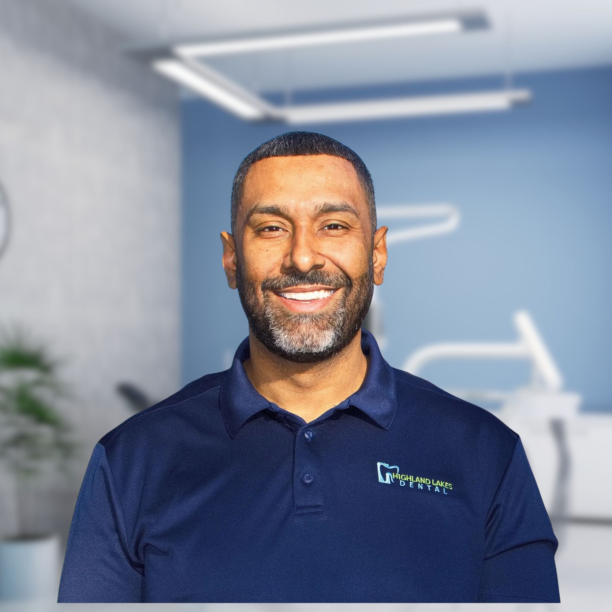 Close-up of a smiling man wearing a navy blue polo shirt with a logo that reads Highland Lakes Dental.