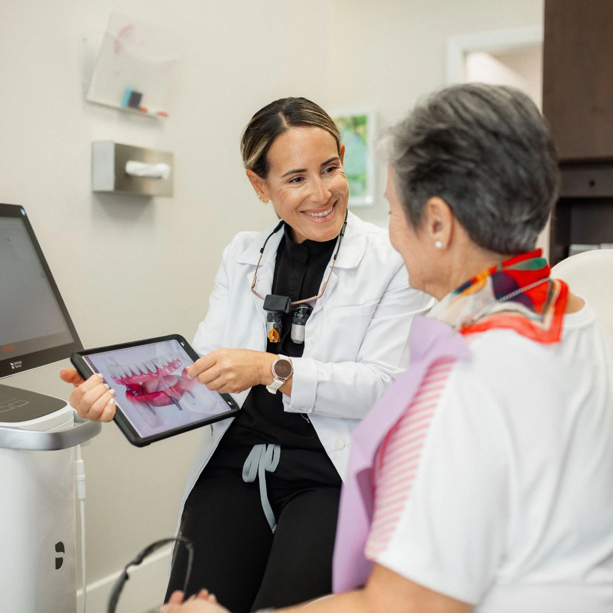 A female healthcare professional shows a digital model of teeth to an elderly woman in a medical office.