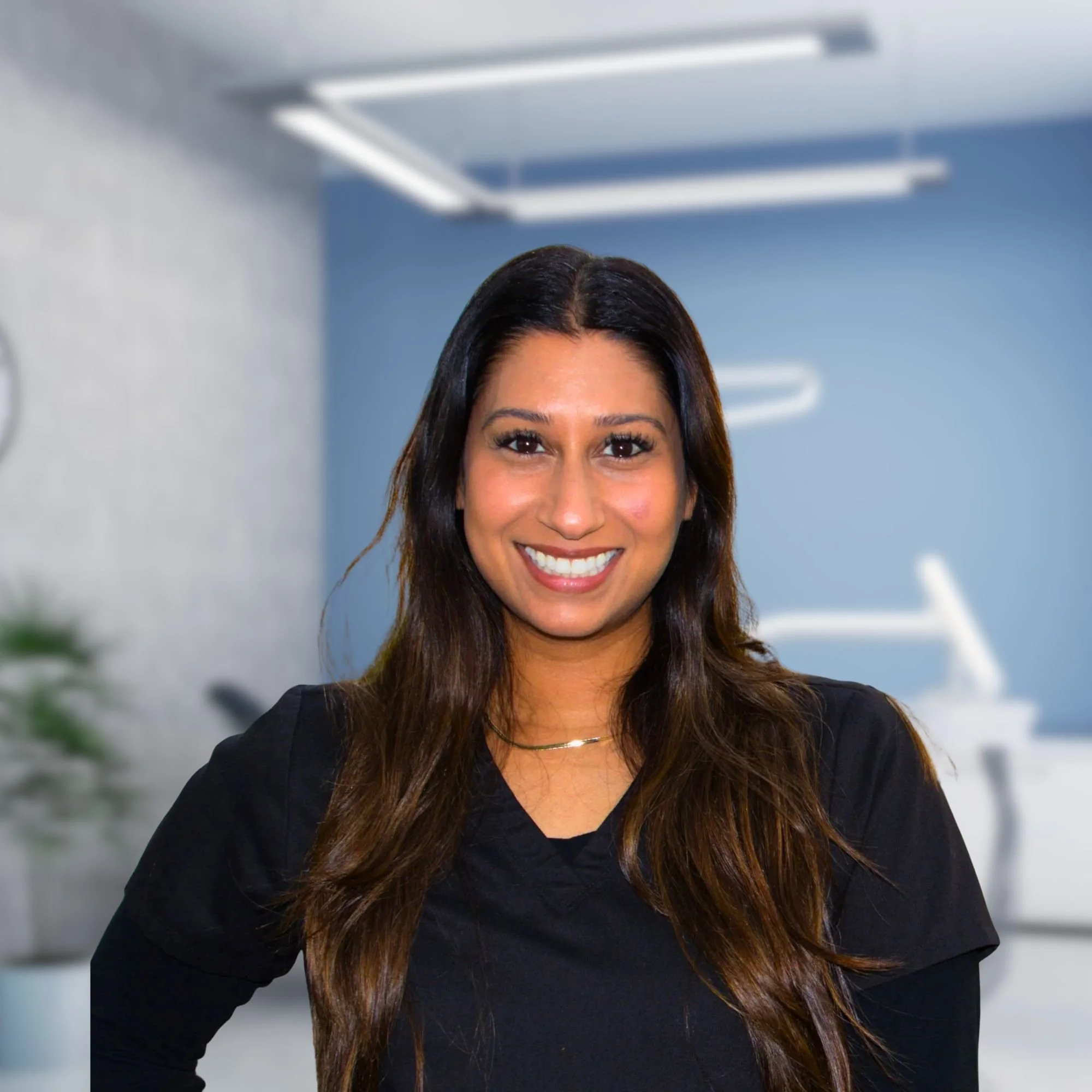 A woman with long, brown hair smiling at the camera, wearing a black top in an indoor office environment.