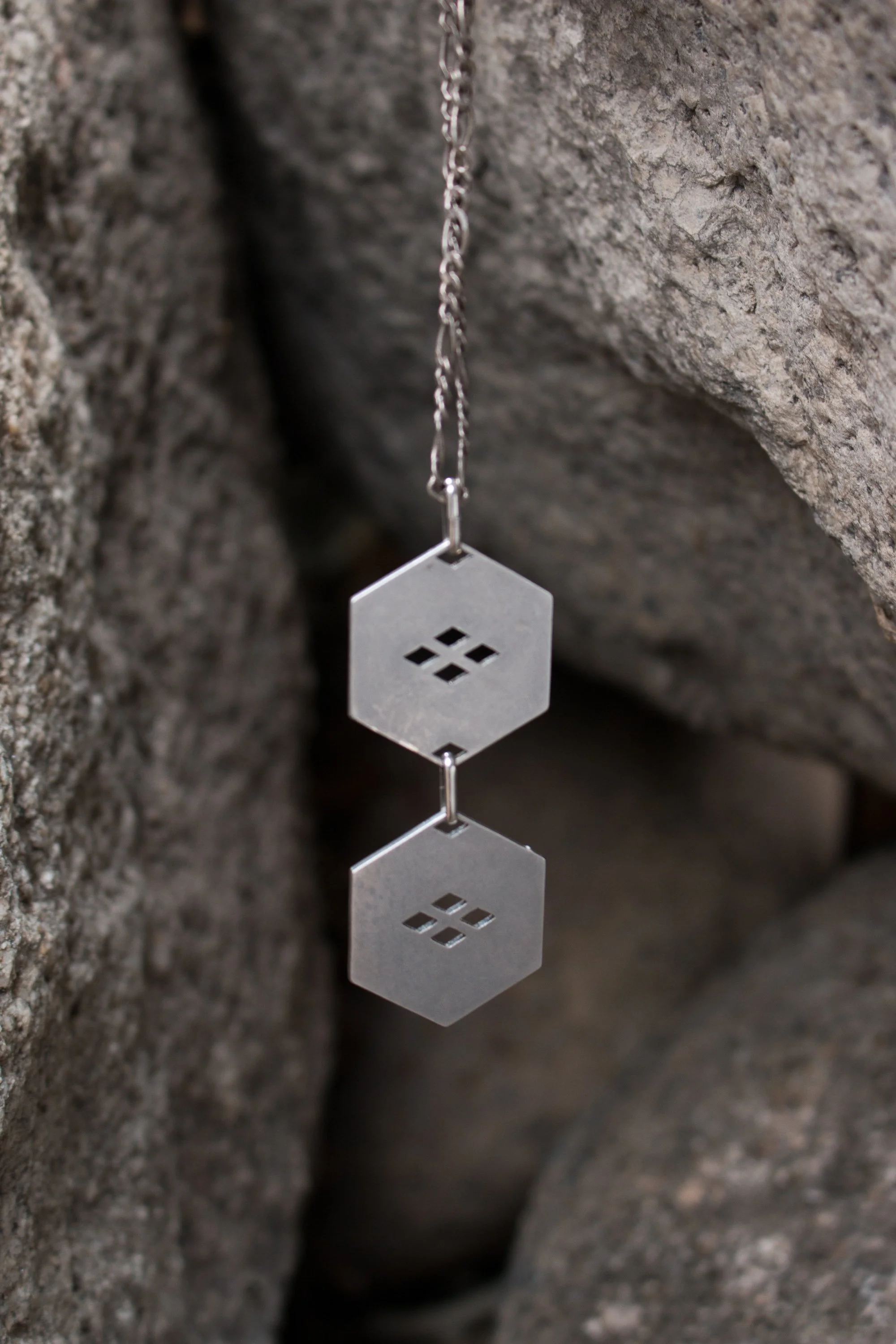 The pendant hanging between boulders, showing the figaro chain and the proportions of the linked hexagons.