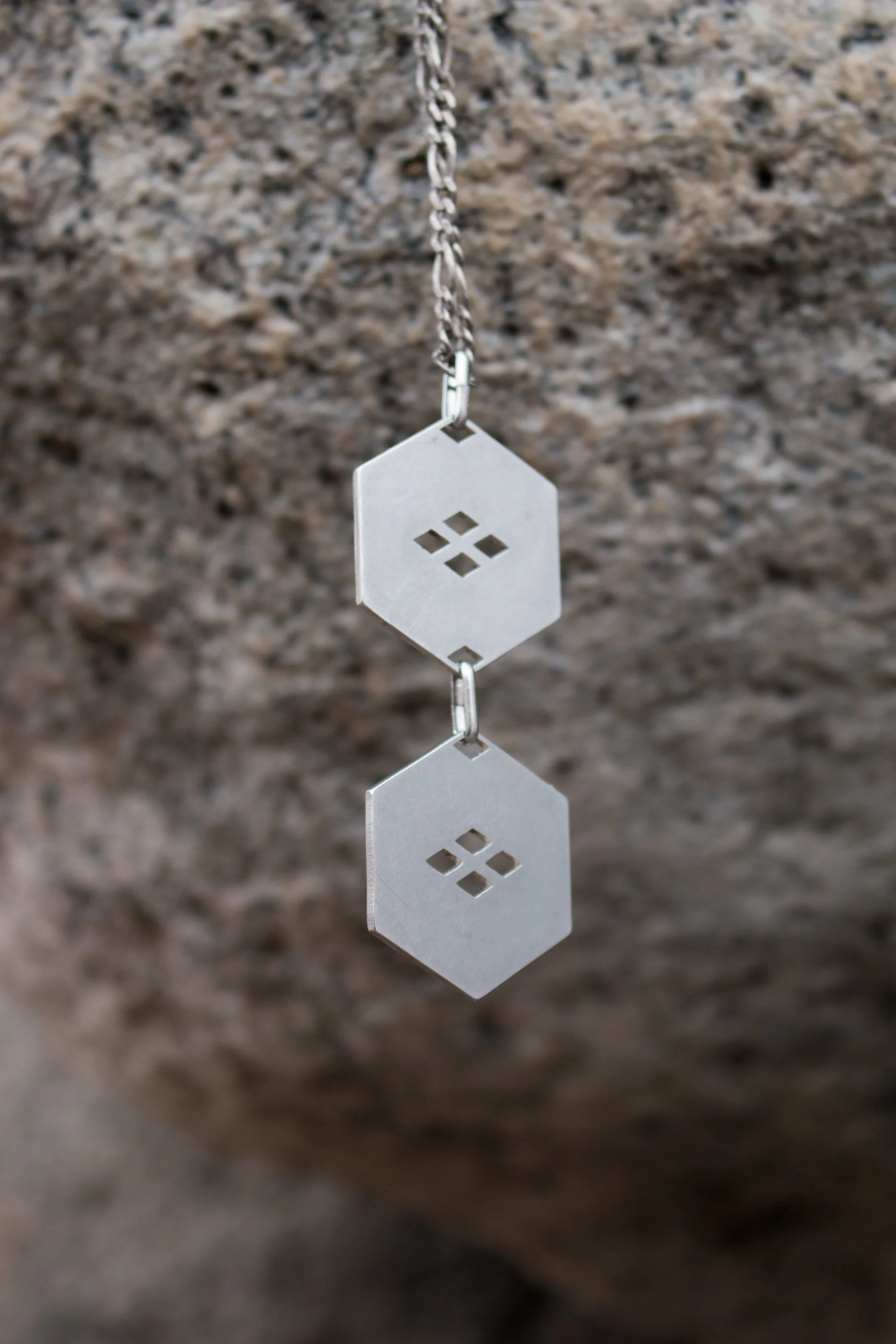 Close view of the pendant hanging against weathered stone, showing the geometric cut-out detail.