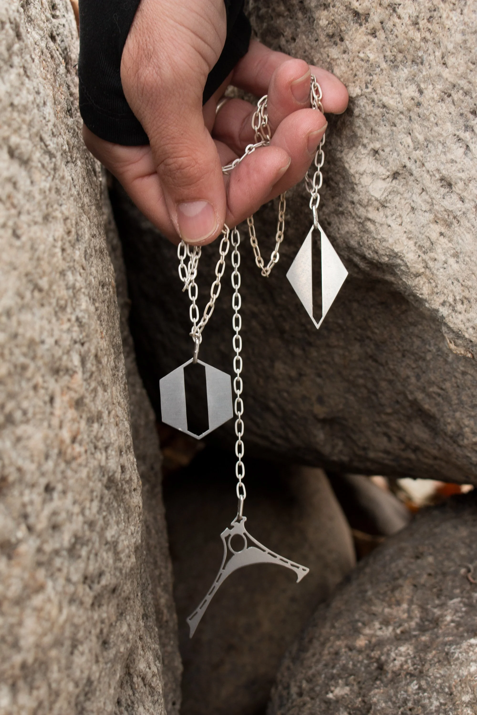 Three pendant designs from the studio held together against stone, showing the diamond pendant alongside related work.