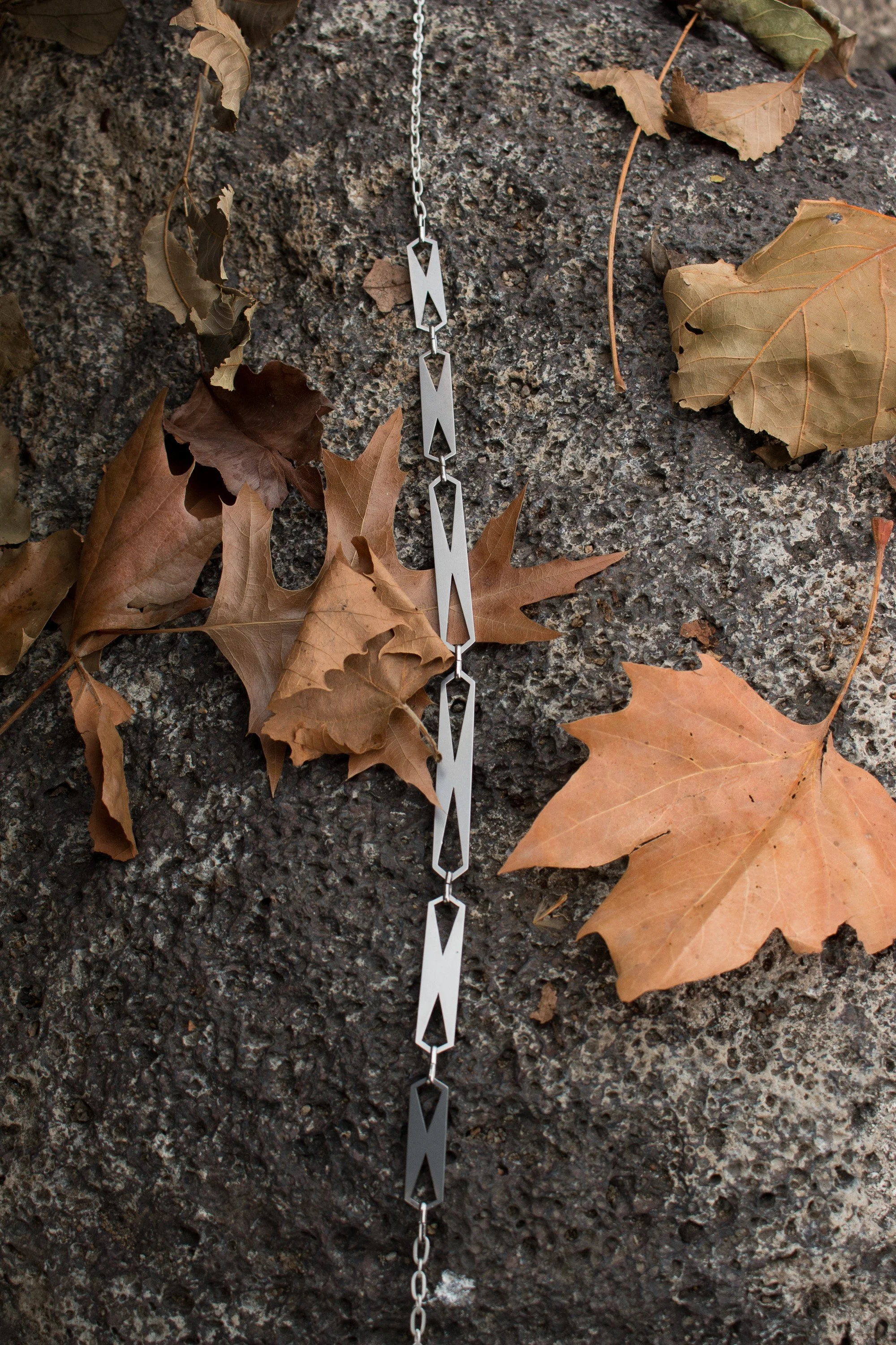 The bracelet laid flat on stone surrounded by autumn leaves, showing full length and link pattern.