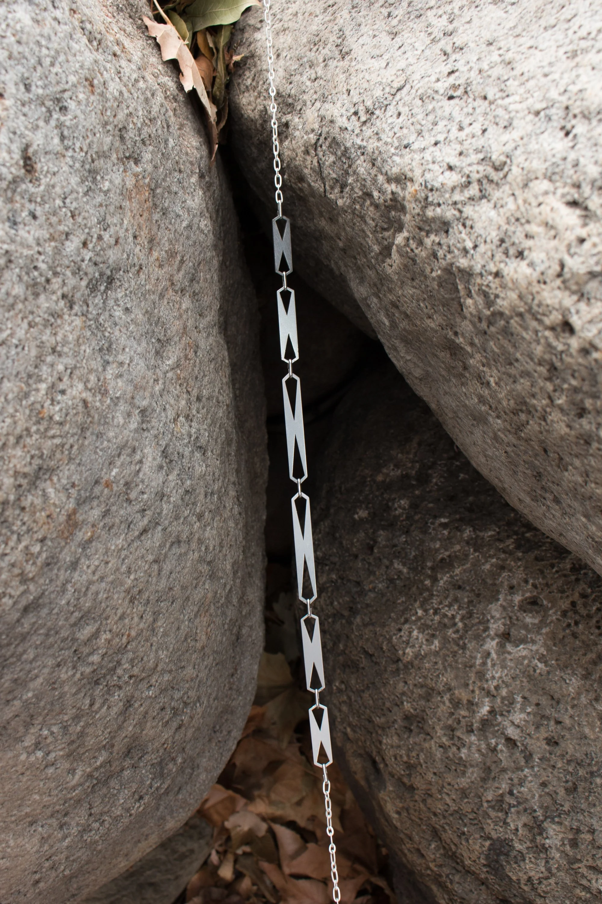 The bracelet hanging vertically between stone, showing the linked plates and X-shaped cut-out detail.