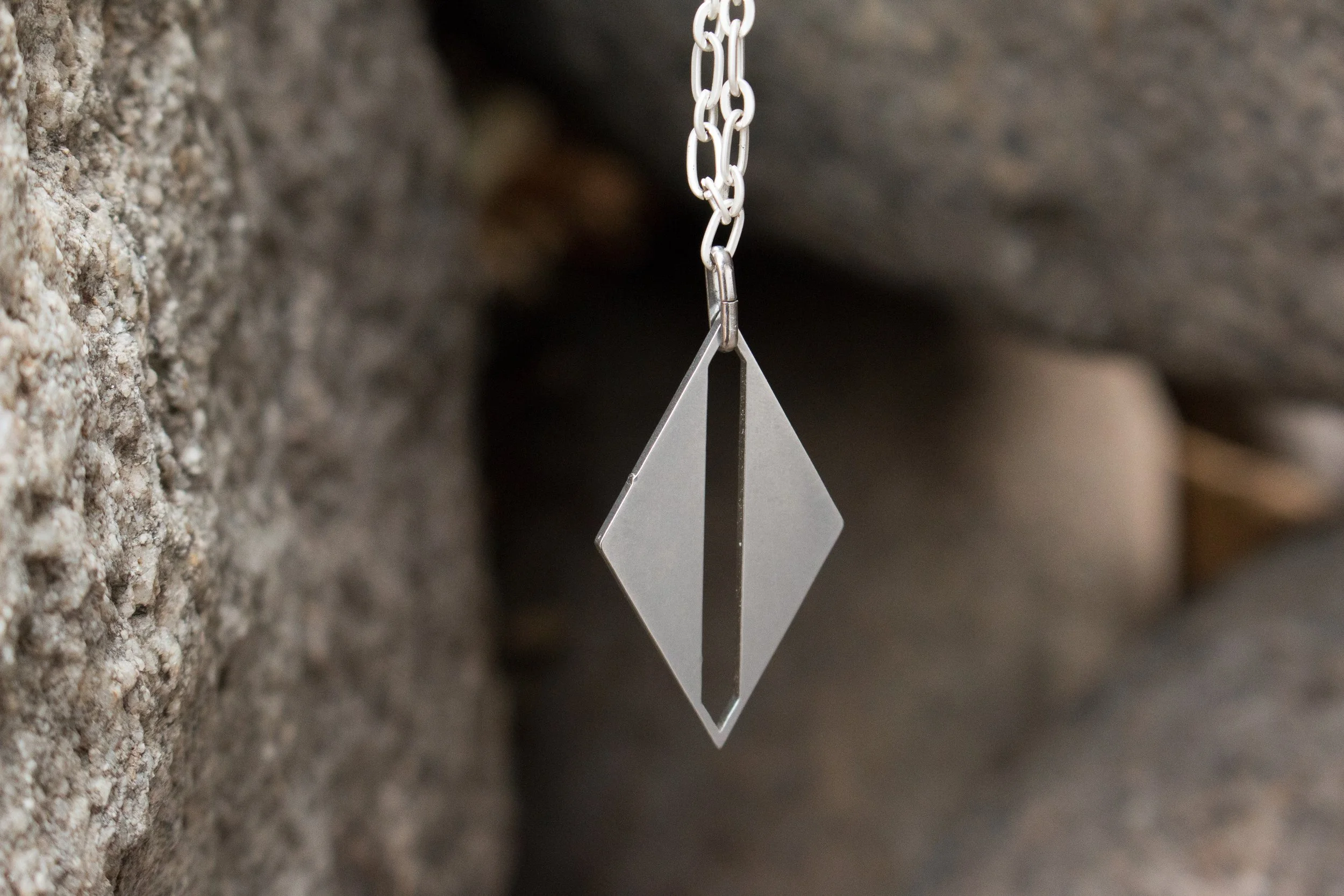 The pendant hanging from a fine cable chain against soft-focus stone, showing the elongated diamond form.