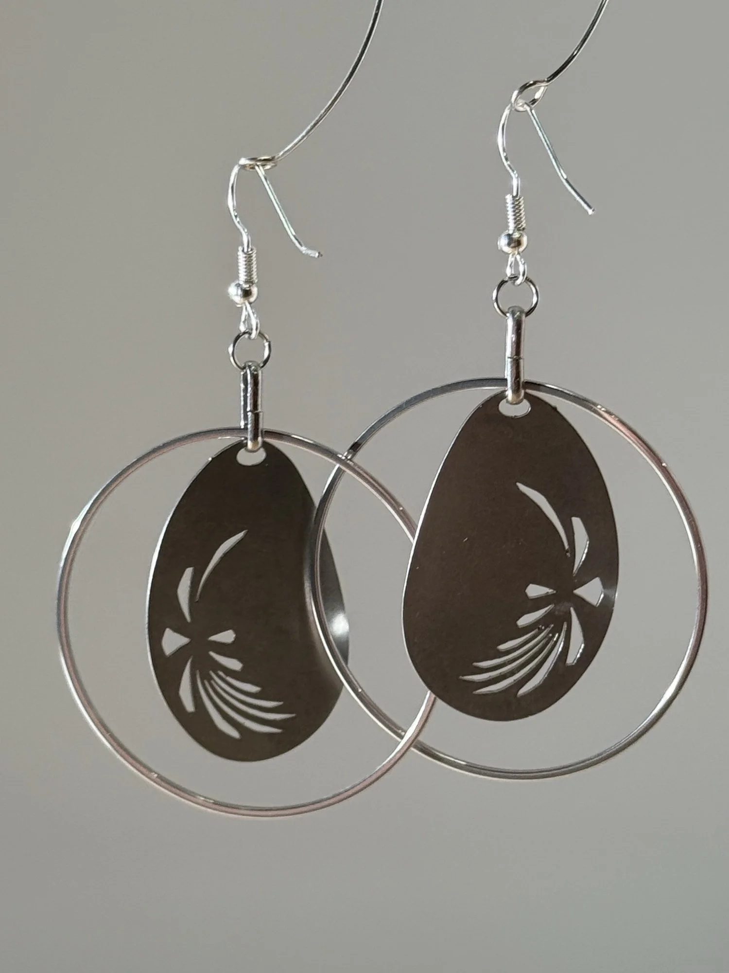 The earrings photographed at an angle on a white surface, showing the interplay of the outer hoop and inner medallion.