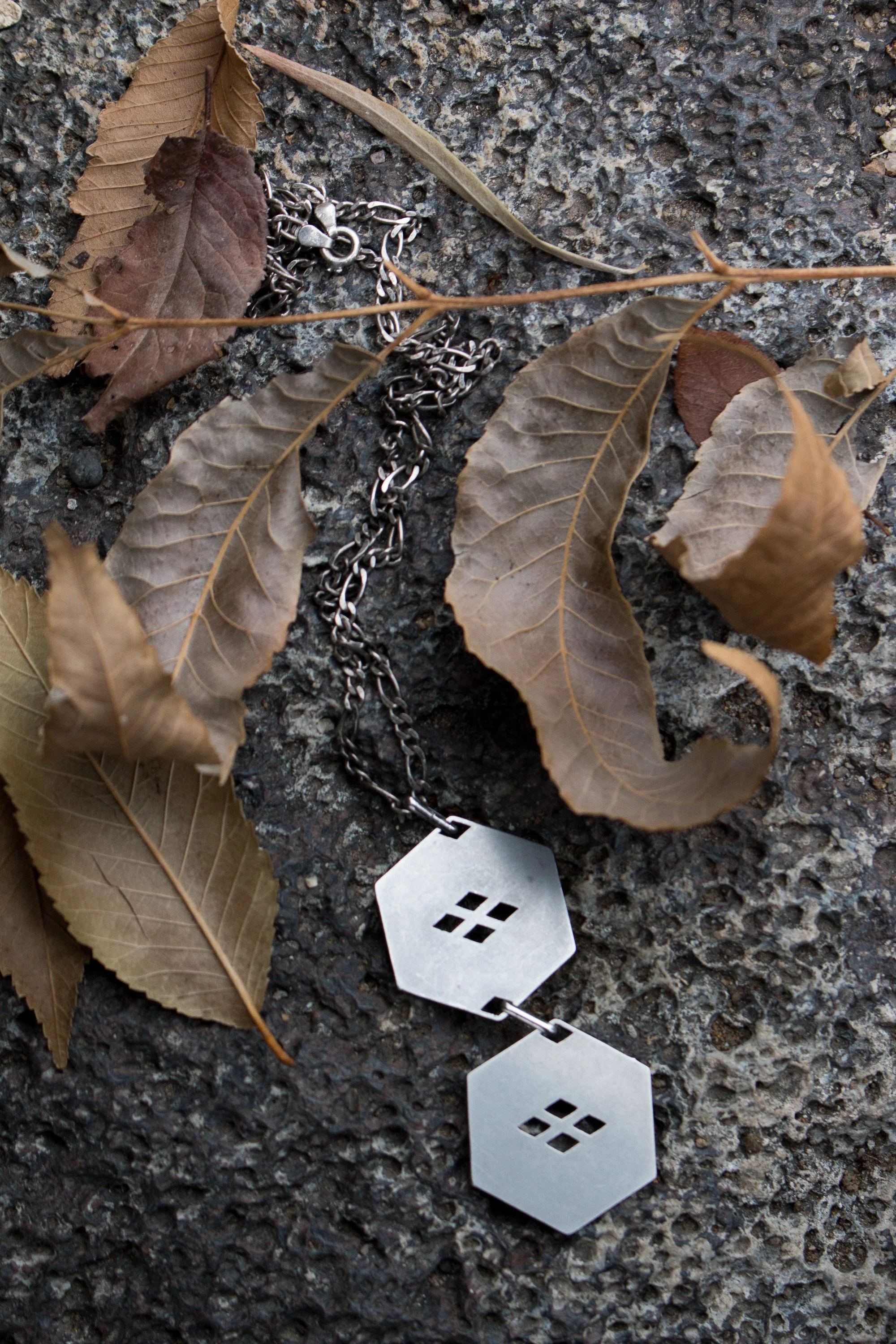 An Older Apotheosis studios hand-made stainless steel jewelry design.  Two hexagons hang in sequence from a twisted chain.  Each hexagon has a japanese heraldic motif cutout.