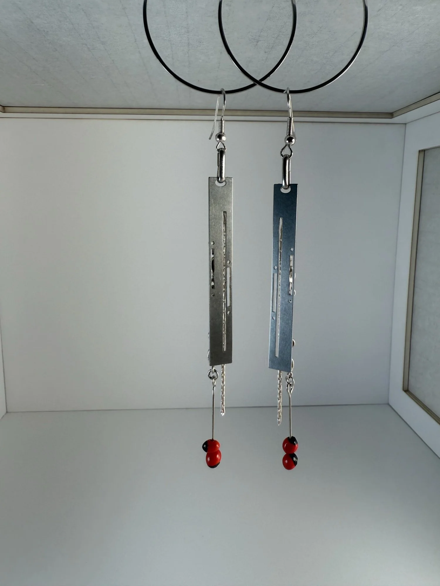 Stainless steel Art Deco earrings with fine chain and red beads, hanging against a white background.