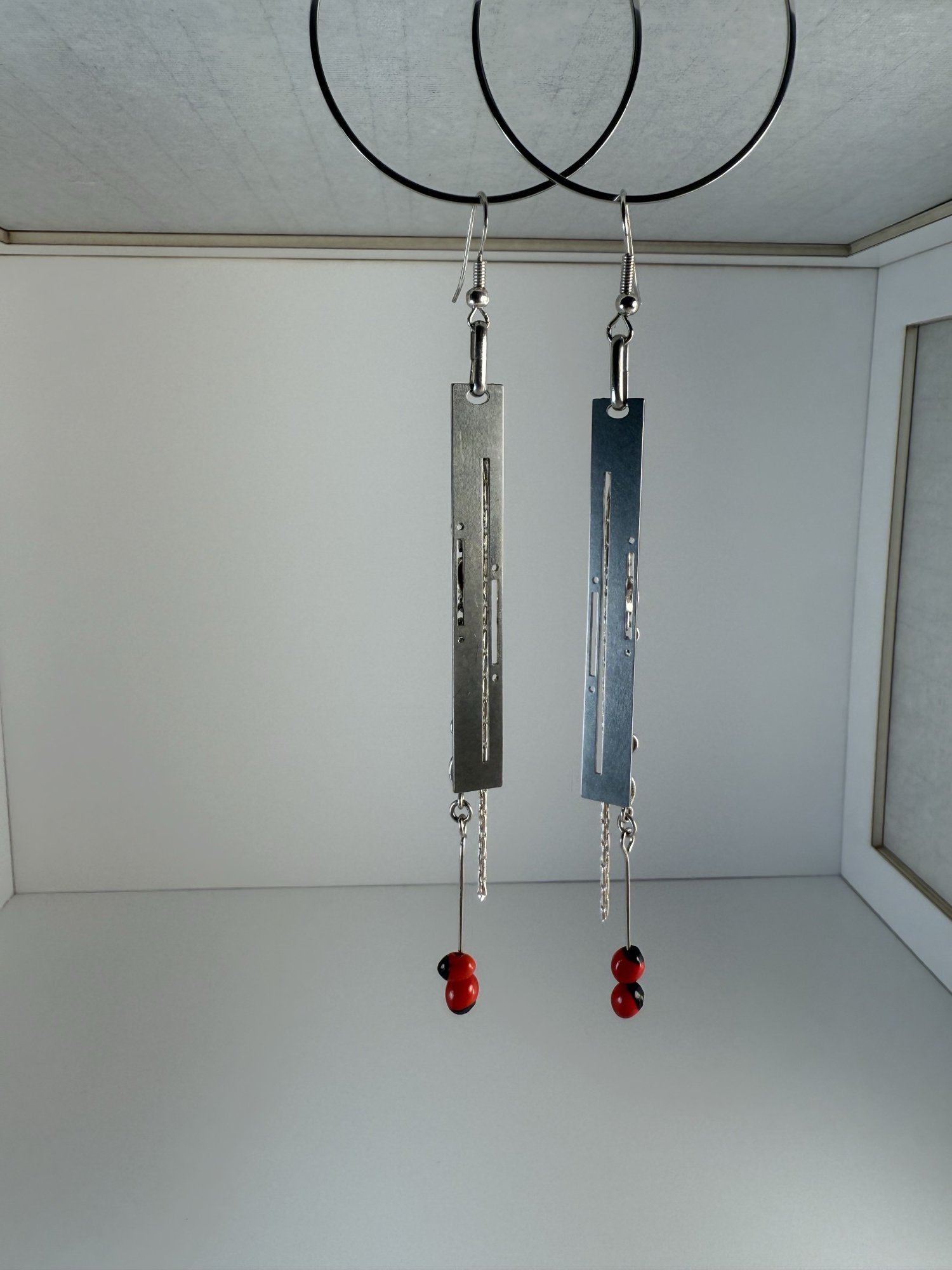 Stainless steel Art Deco earrings with fine chain and red beads, hanging against a white background.