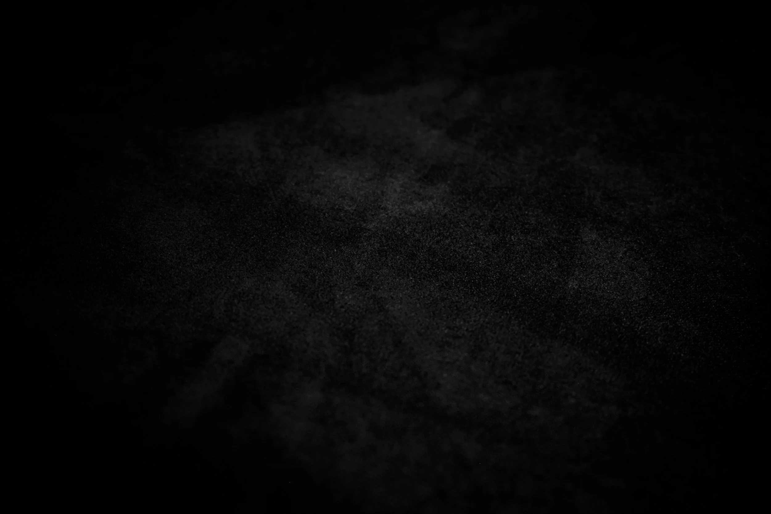 Dark, grainy black surface with faintly visible texture.