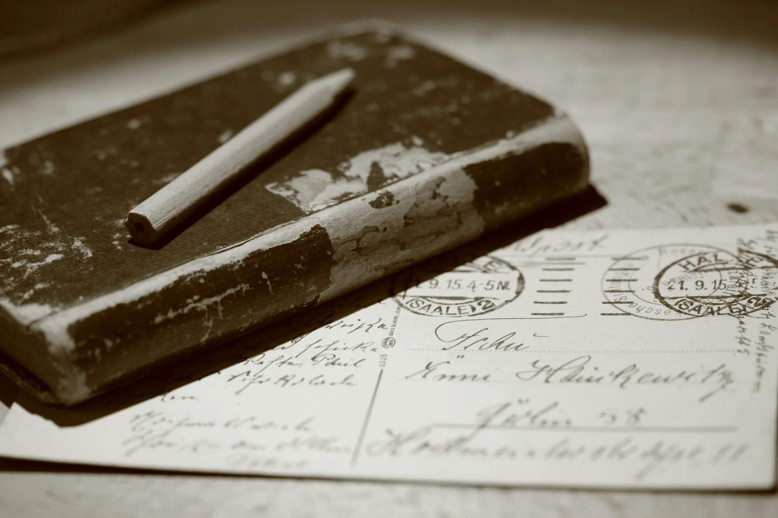 Close-up of an old piece of chalk resting on a weathered blackboard with old handwritten letters and stamps visible underneath.