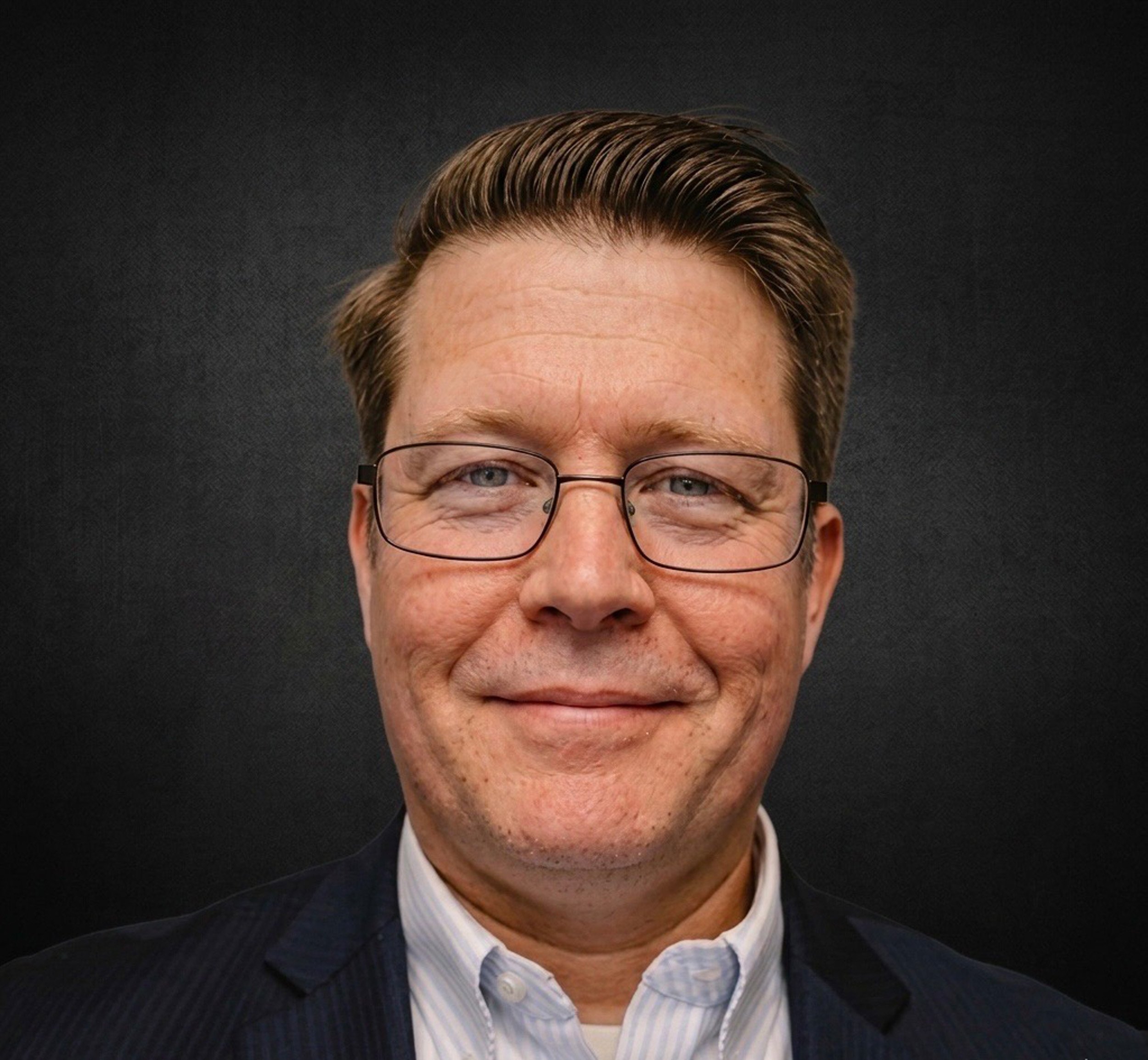 Close-up of a middle-aged man's face with glasses, showing his hair, eyes, and upper part of his face, against a dark background.