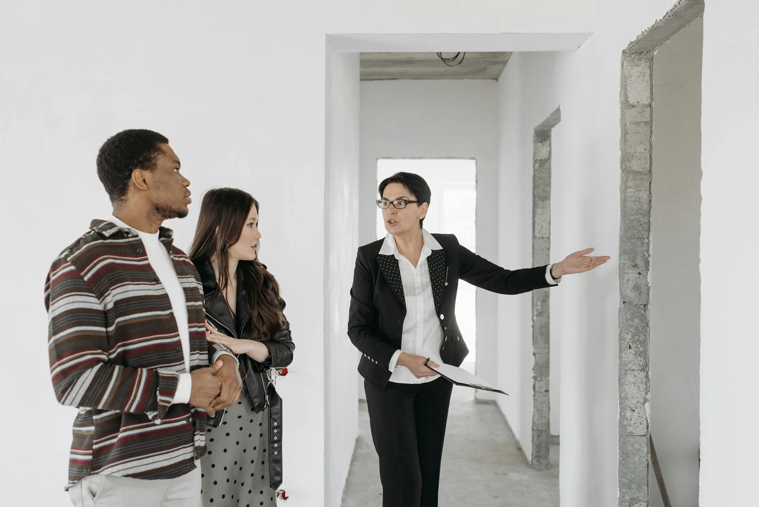 A group of four diverse people, including a woman in professional attire, are engaged in a discussion inside a building under construction or renovation, with unfinished walls and visible brickwork.