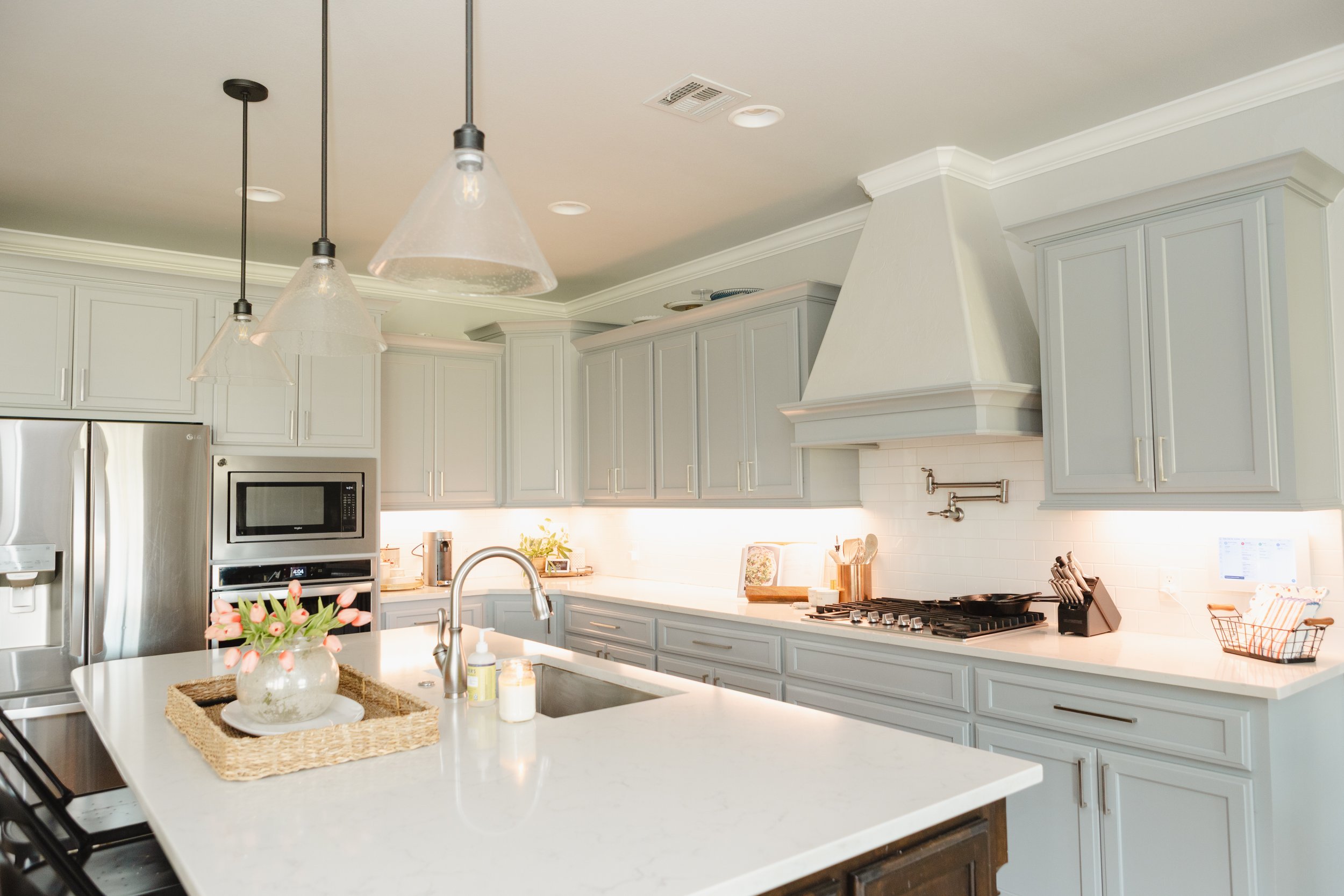 Modern kitchen with white cabinetry, stainless steel appliances, and a white island counter with a vase of pink tulips, pendant lights, and cooking utensils.