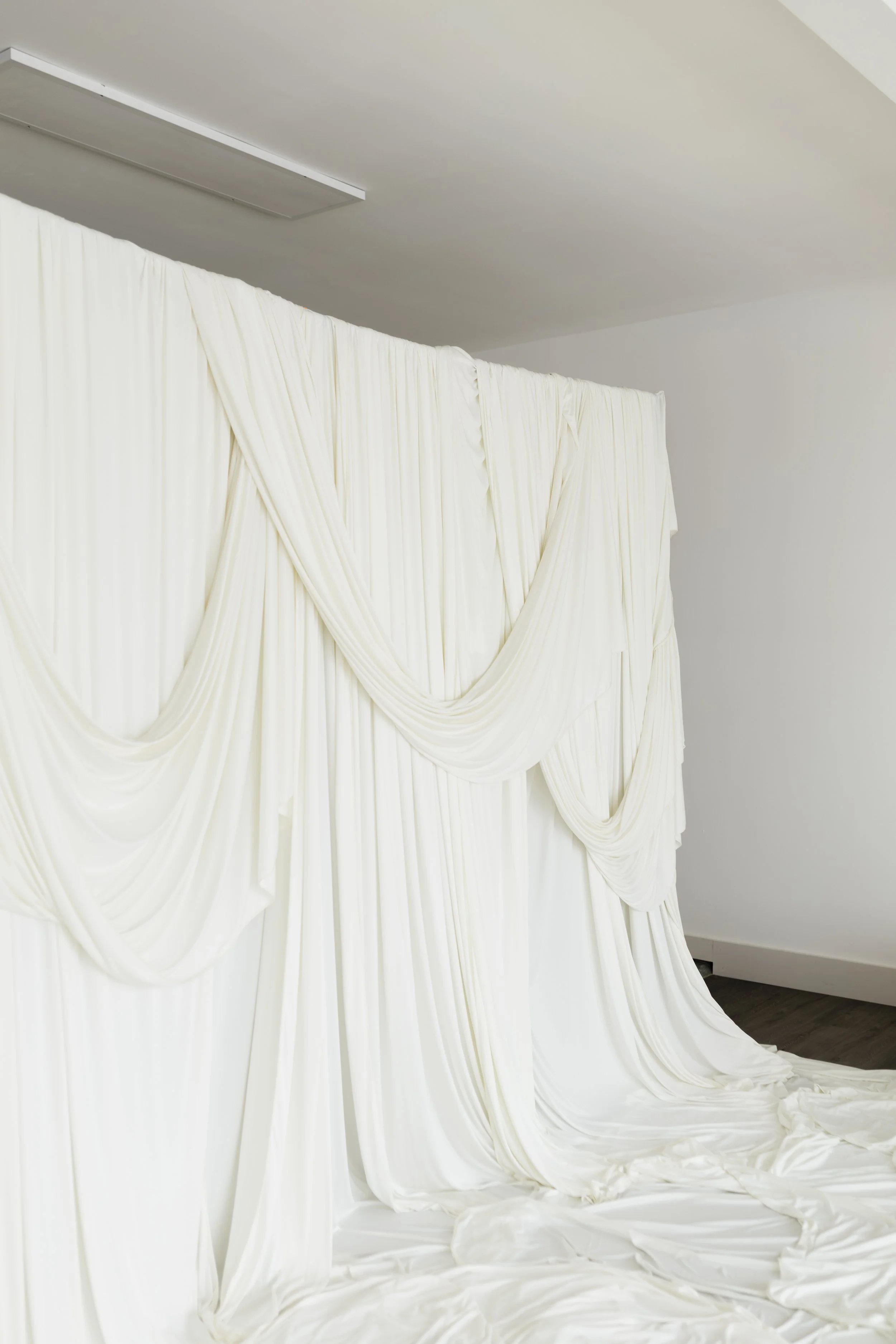 Cream-colored, draped fabric creating a backdrop on a wall and floor, with a fold extending onto the floor in a minimalist space.