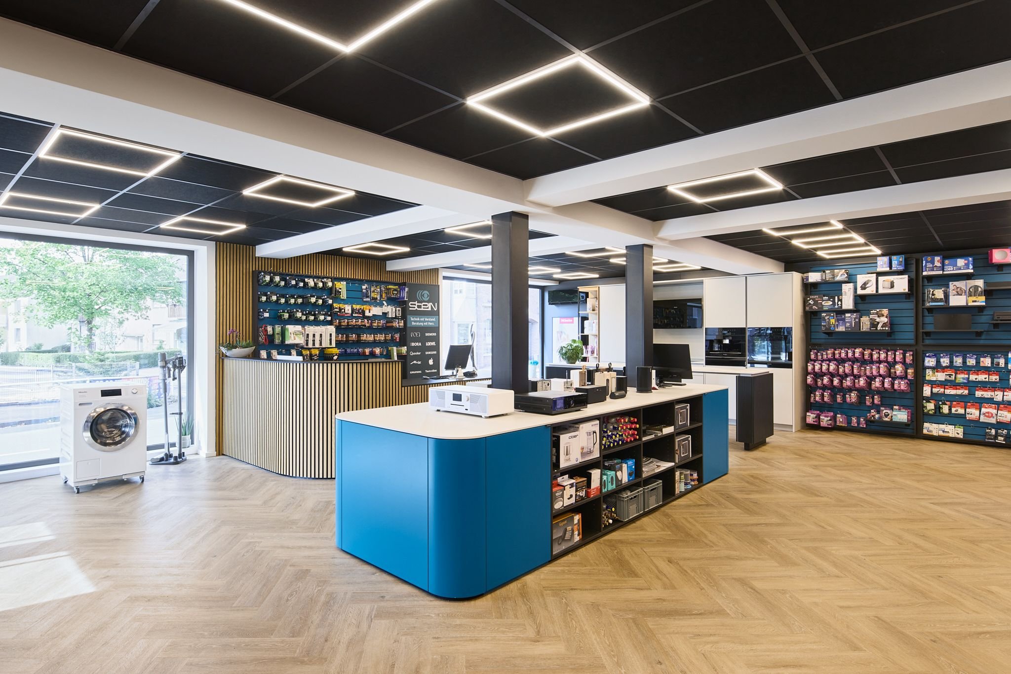 Innenansicht des Elektronikfachgeschäfts Radio Stein in Ratingen mit dunklem Deckenlicht, Regal mit Elektronikzubehör und weißen Wänden.