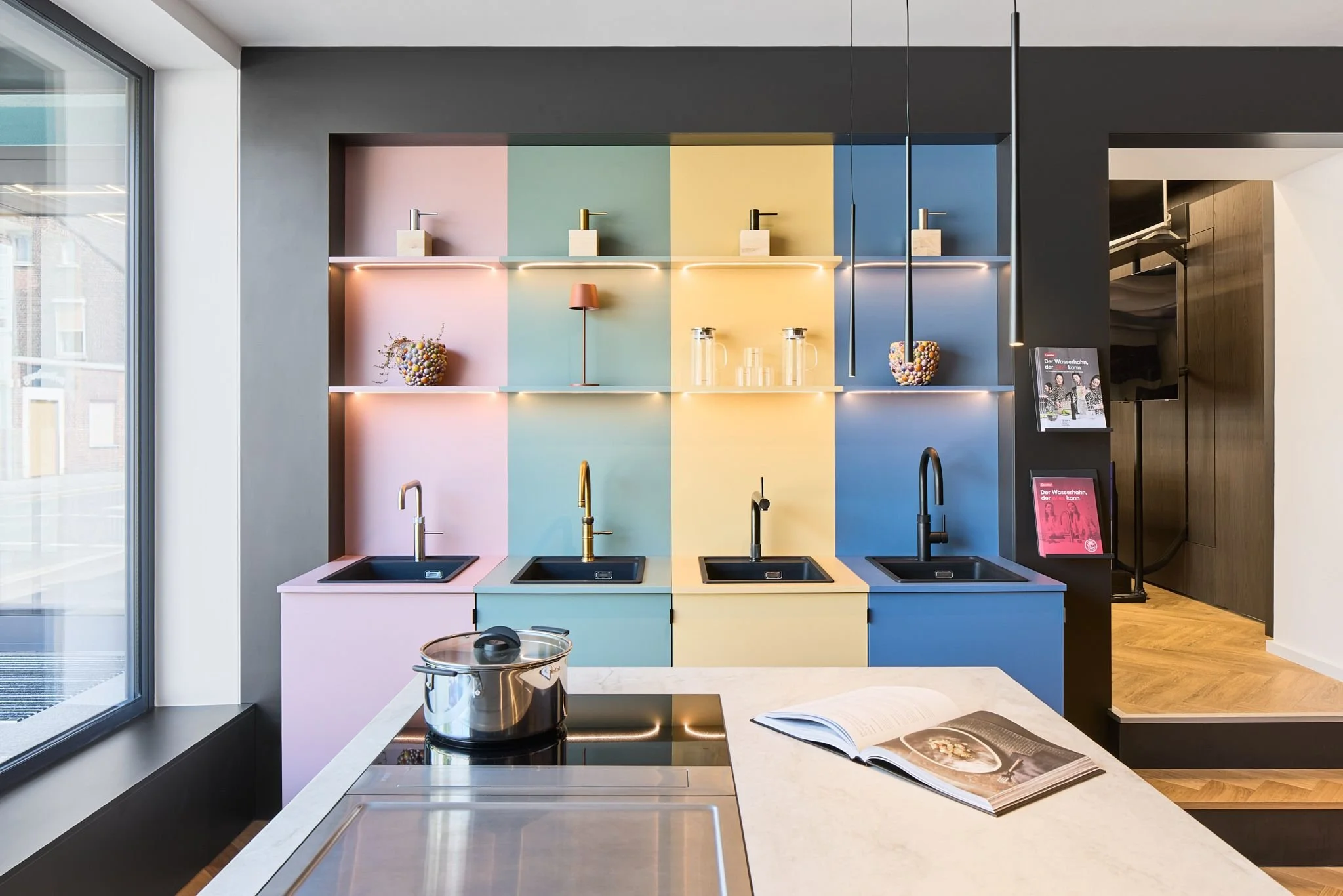 Moderne Küche mit bunten Wandpaneelen, Kochendwasser-Armaturen von Quooker und Blanco, offenen Regalen mit Dekorationen, Kochbuch und Kochutensilien.