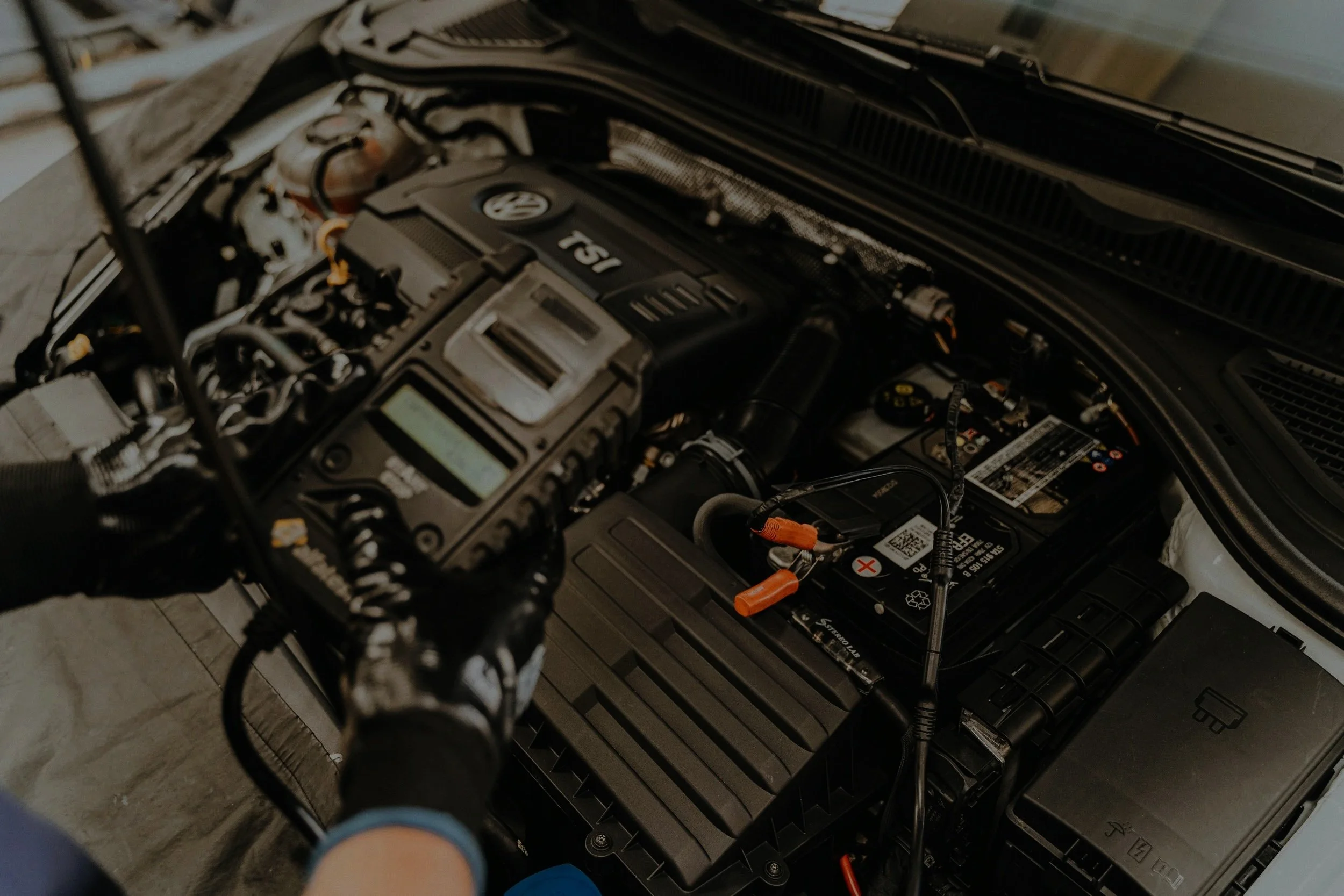 View of a car engine bay with various components, including a visible Toyota logo and T5I on the engine cover, and a person's hand and foot in the foreground.