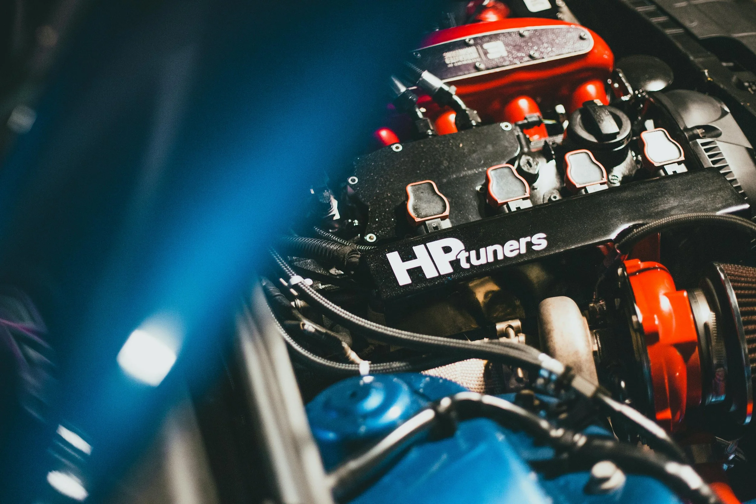 Close-up of a car engine with red components and a bumper sticker reading 'HP tuners'.