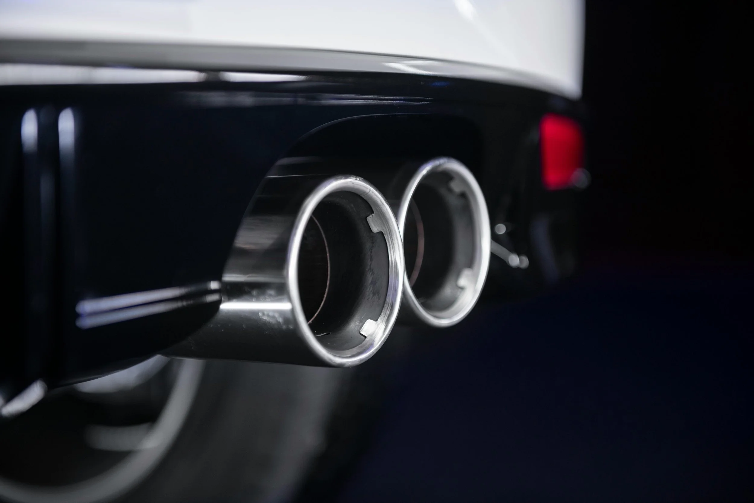 Close-up of a car's dual exhaust pipes with a black background and part of the bumper visible.