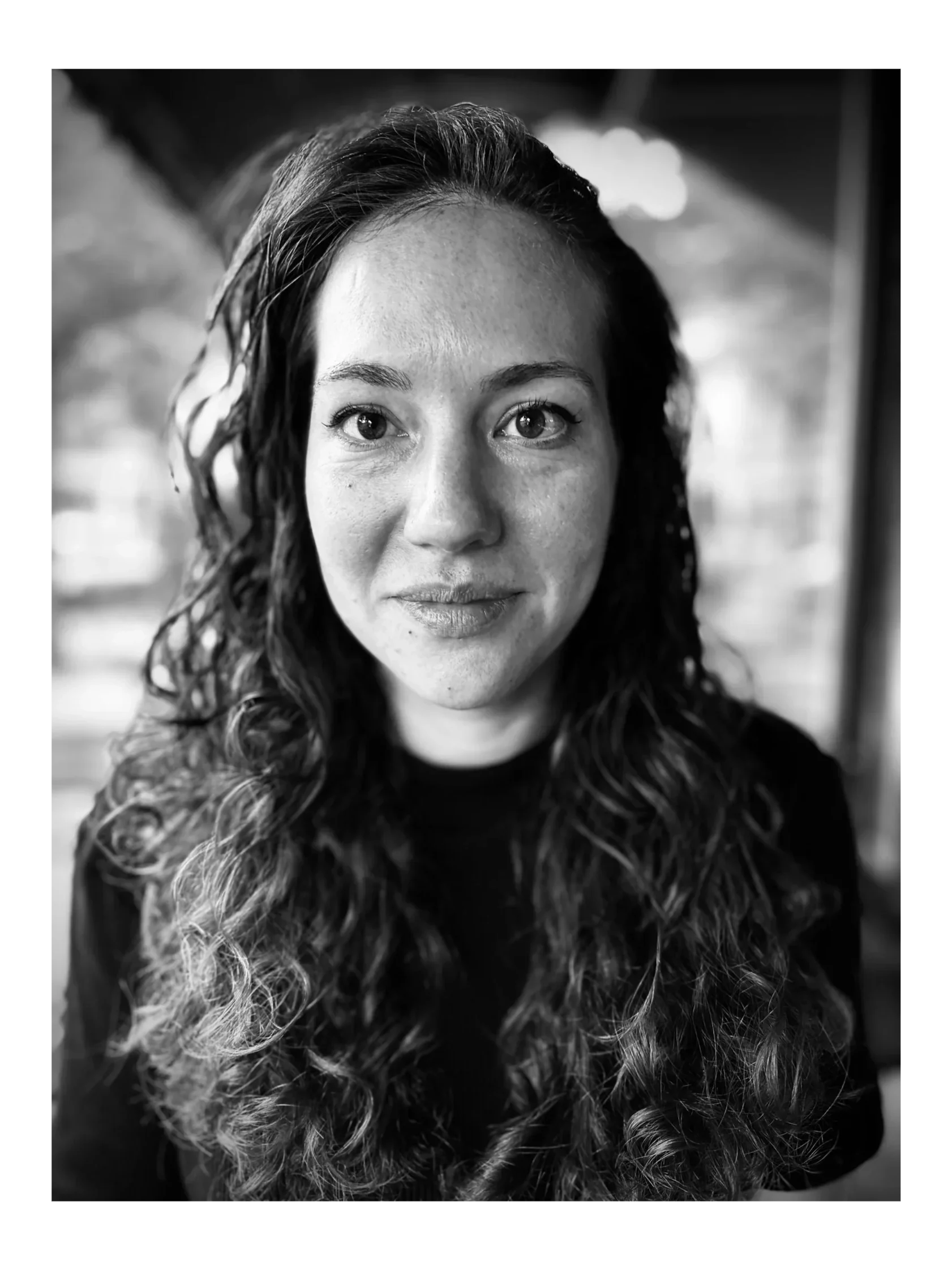 Close-up black and white portrait of a woman with curly hair, looking at the camera with a slight smile.