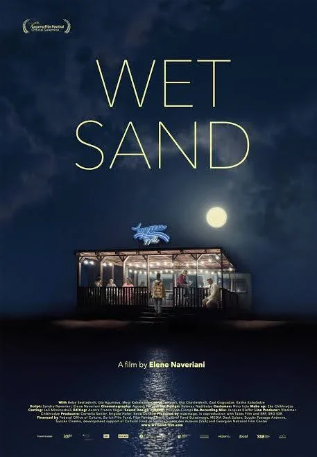 Movie poster for 'Wet Sand' shows a nighttime scene with a full moon, a dark sky, and a building with a neon sign that says 'happy hour.' The film title appears in large yellow letters at the top, and there are people inside and outside the building 