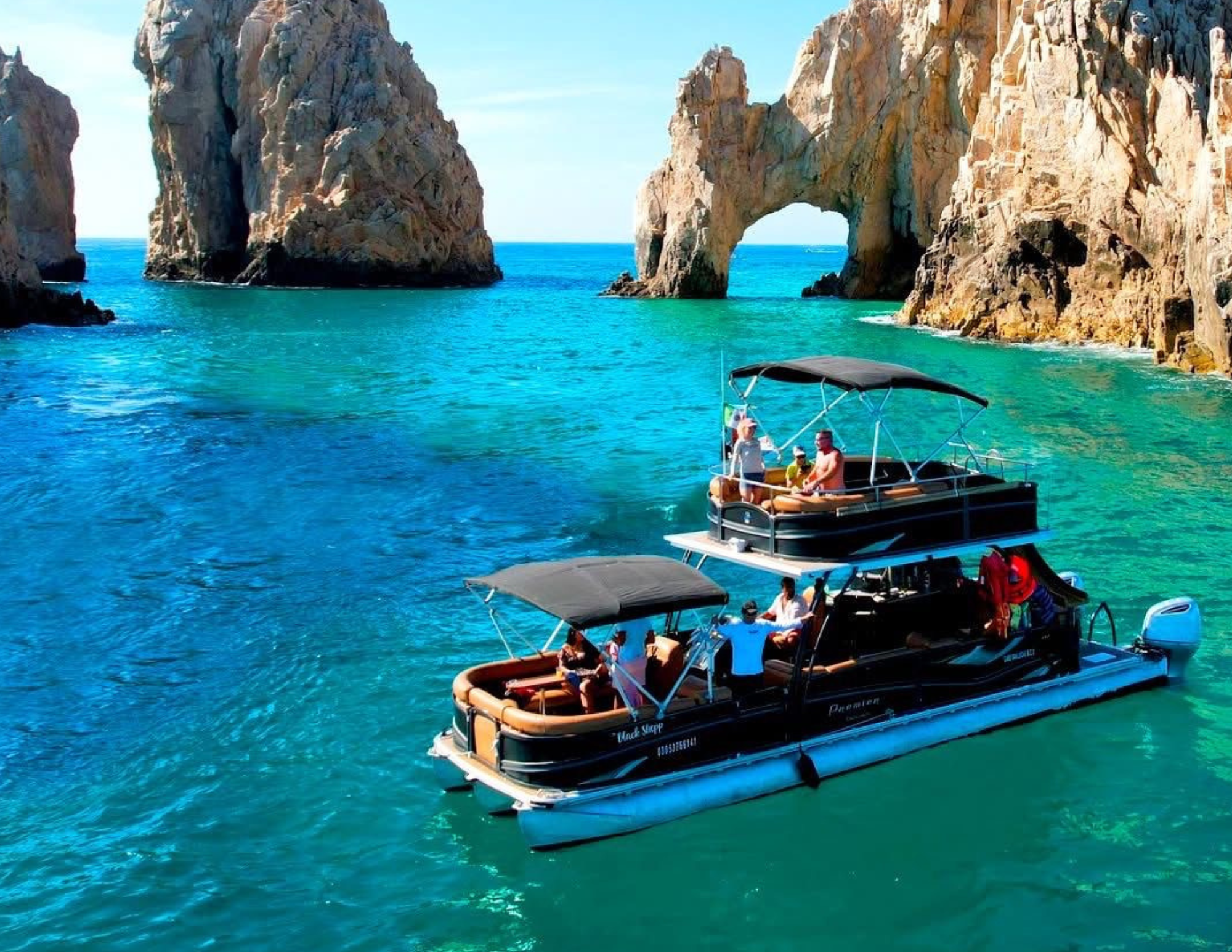 A group of people enjoying a boat ride near rocky cliffs with a natural sea arch formation.