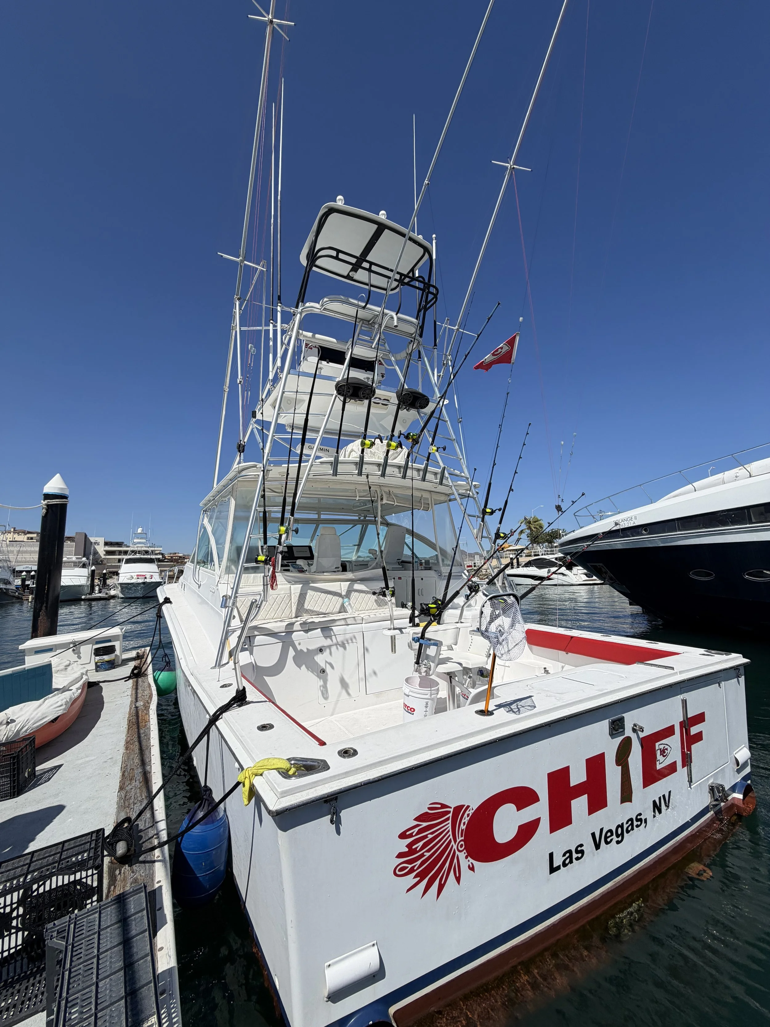 A white fishing boat docked at a marina with multiple fishing rods attached to the boat, a Canadian flag flying, and the text 'CHIEF LAS VEGAS, NV' on the side.