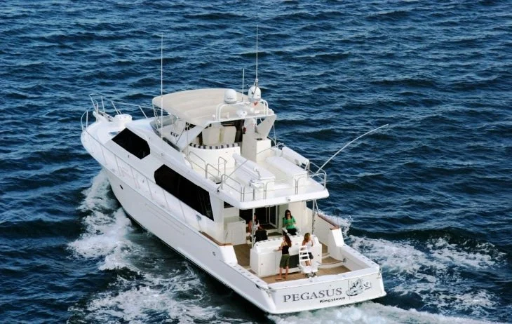 A white yacht labeled 'PEGASUS' cruising in blue ocean water with people on deck.