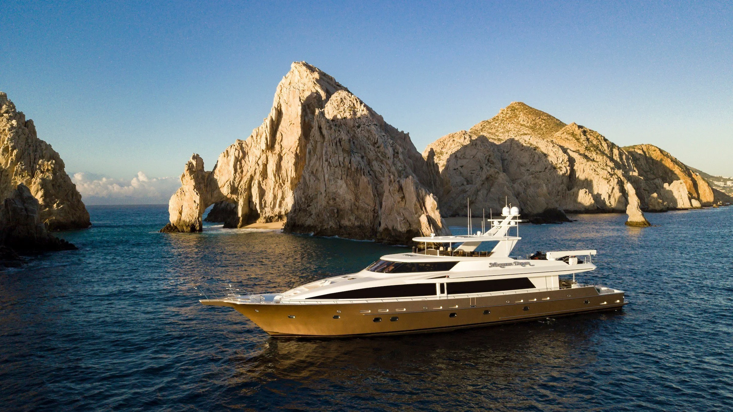 A luxury yacht sailing near large rocky cliffs and sea caves under a clear blue sky.
