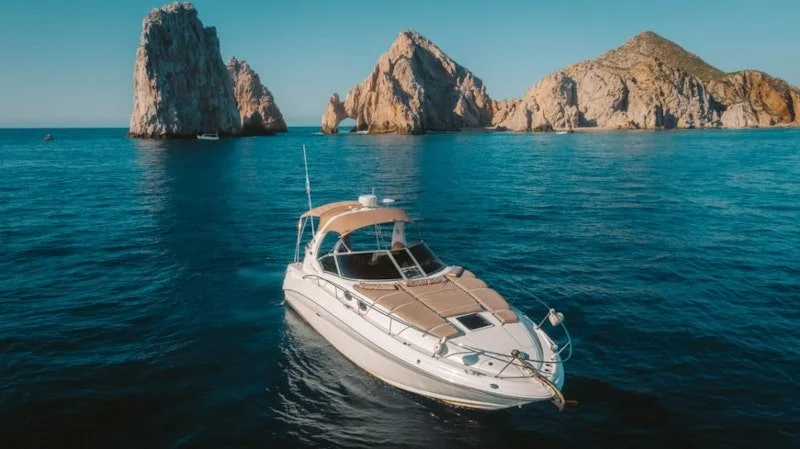 A yacht sailing in blue water near rocky islands with clear skies.