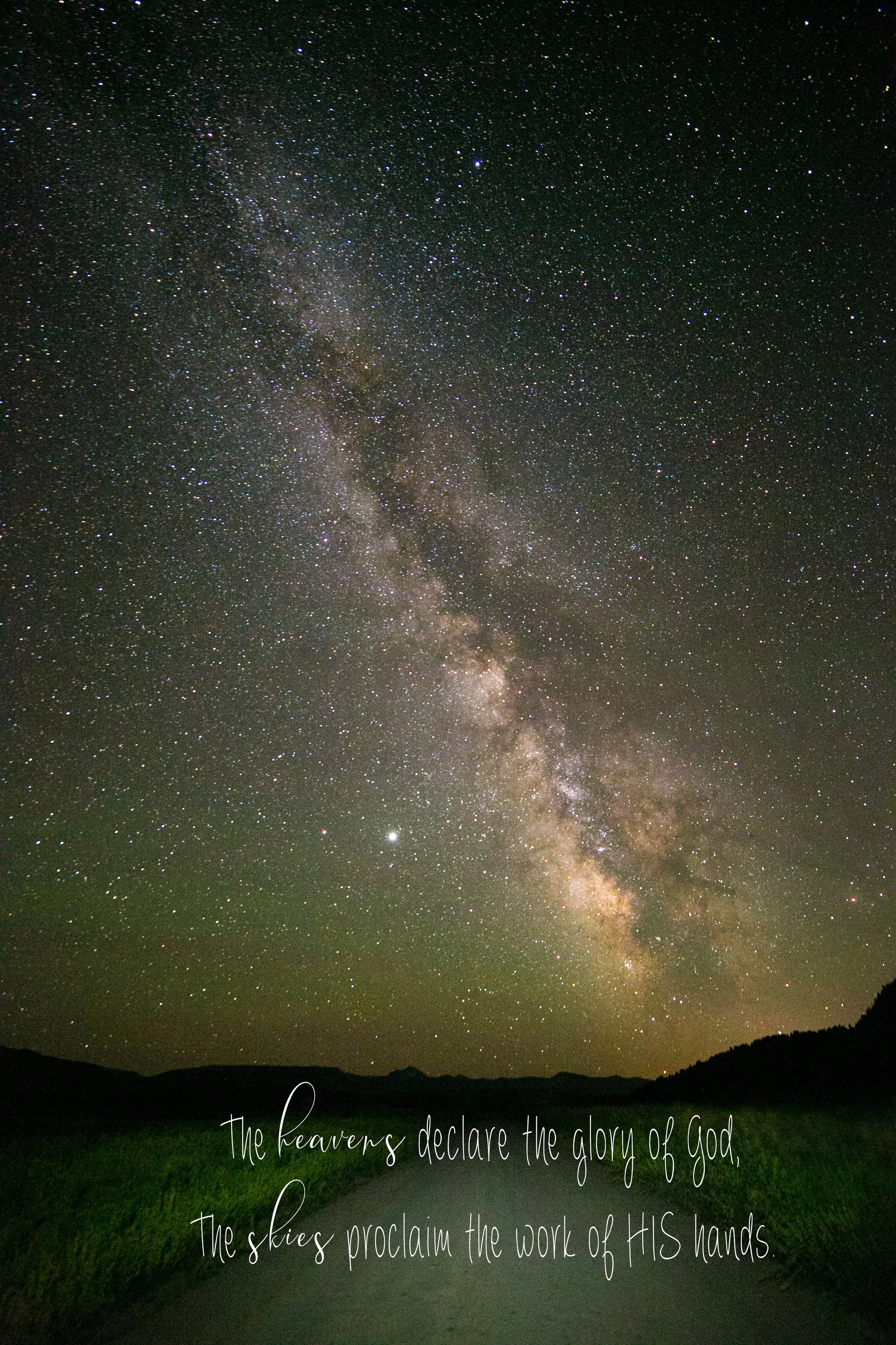 Night sky filled with countless stars and the Milky Way galaxy over a silhouette of mountains and a grassy landscape, with overlaid inspirational text in cursive writing.