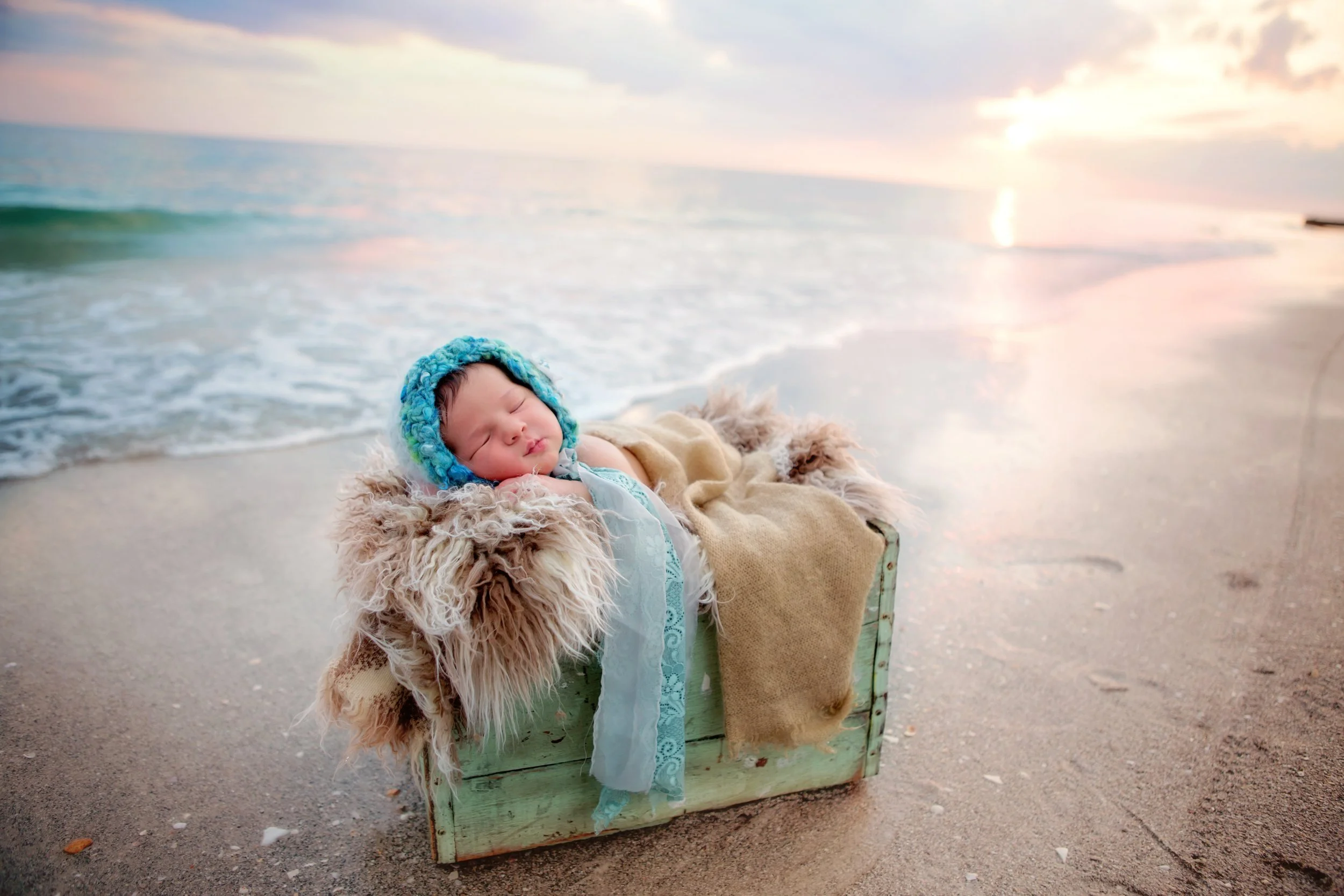 A young child sleeping in a cozy basket at the beach during sunset.