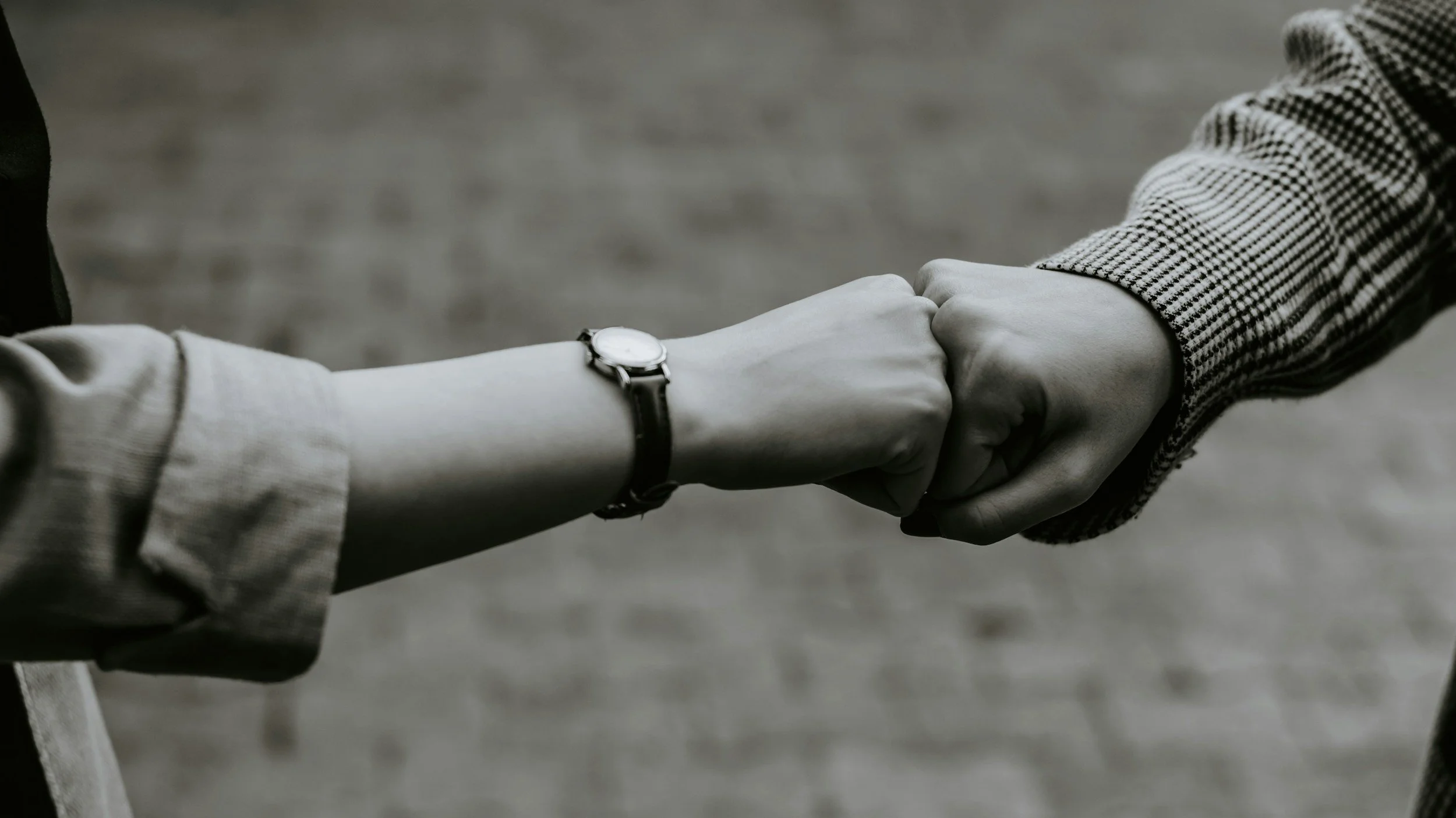 Two people shaking hands, one wearing a watch and a striped jacket, the other in a plain sleeve, in black and white.