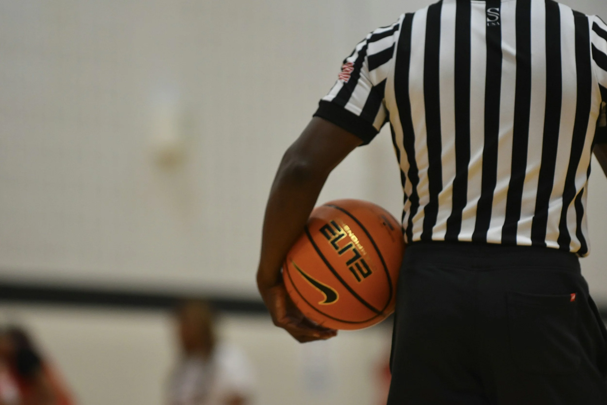 Person in black and white striped shirt holding an orange basketball.
