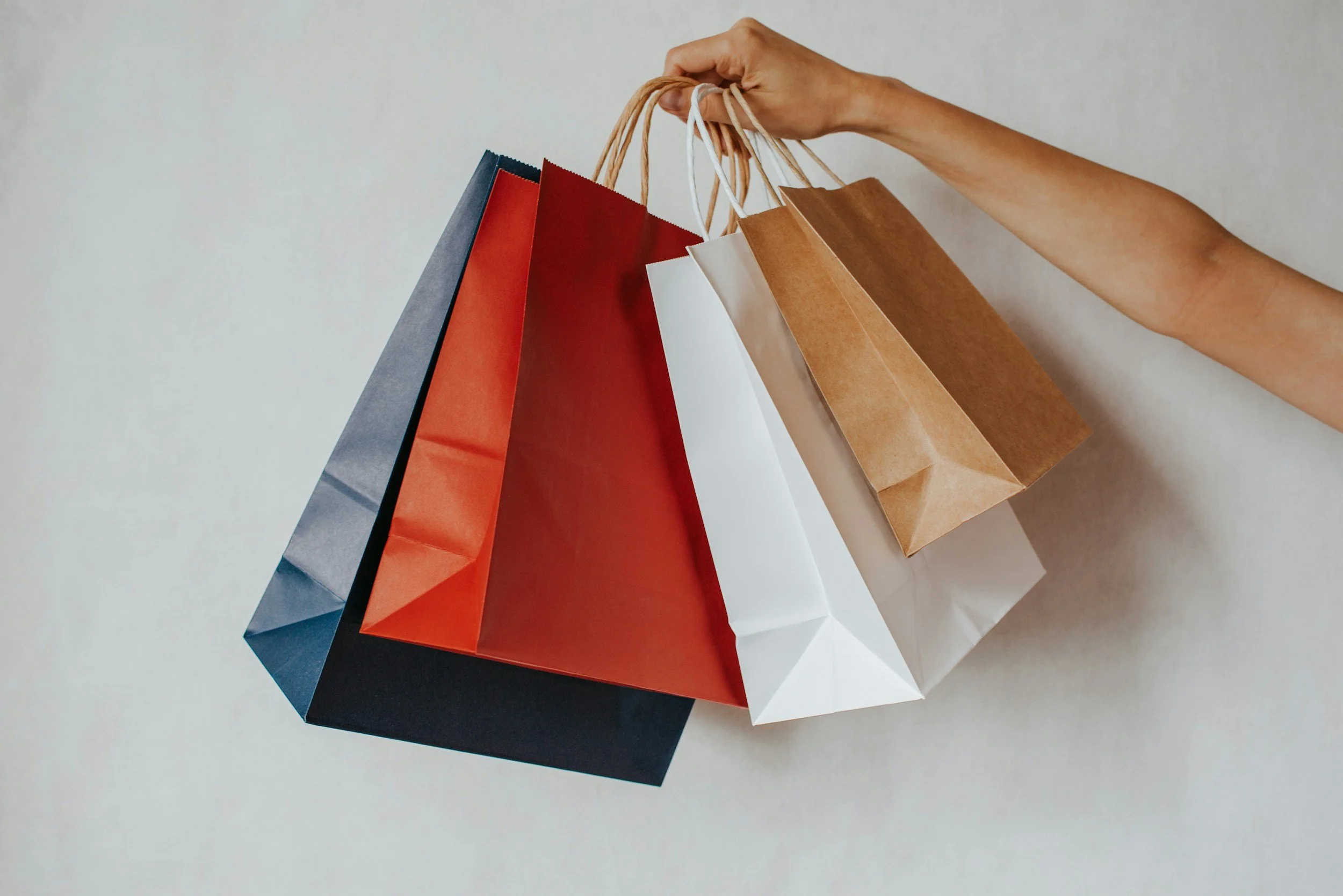 Various colorful shopping bags hanging from a person's hand.