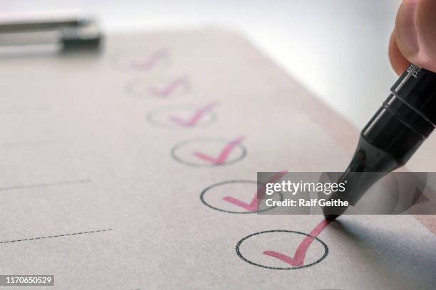 Close-up of a black marker marking checkmarks in pink inside circles on a checklist paper.