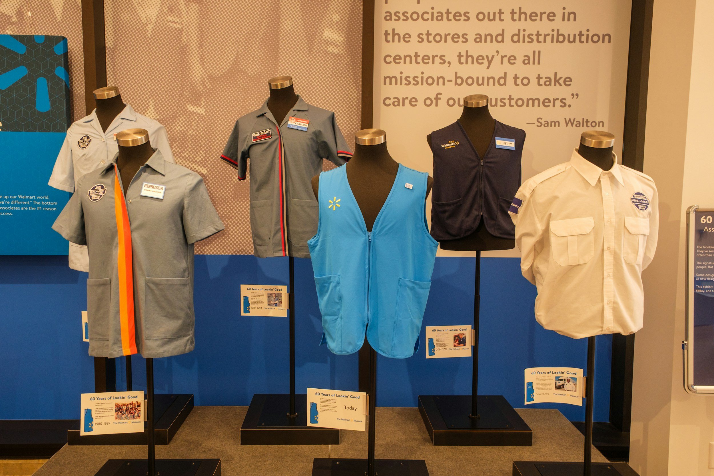 Display of vintage Walmart uniforms on mannequins, including shirts and vests, with informational plaques about Walmart's history and mission.