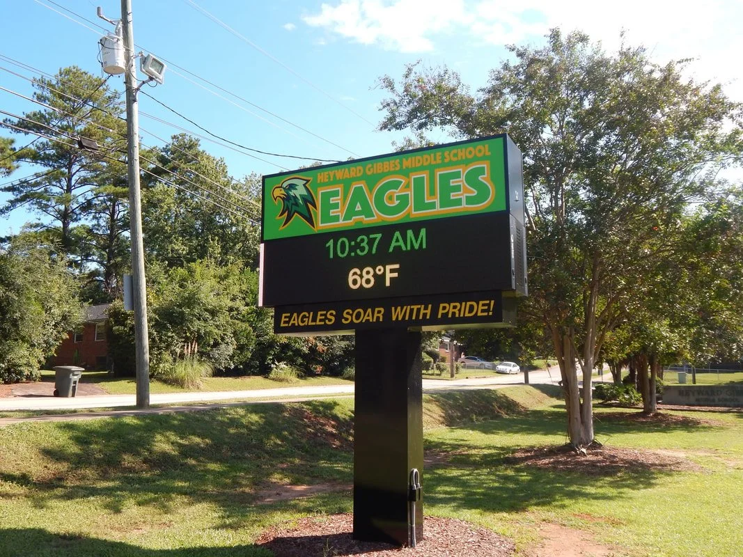 Digital sign outside Meyward Gibbs Middle School displaying the school name, mascot 'Eagles', current time 10:37 AM, temperature 68°F, and the slogan 'Eagles soar with pride' amid trees and power lines.