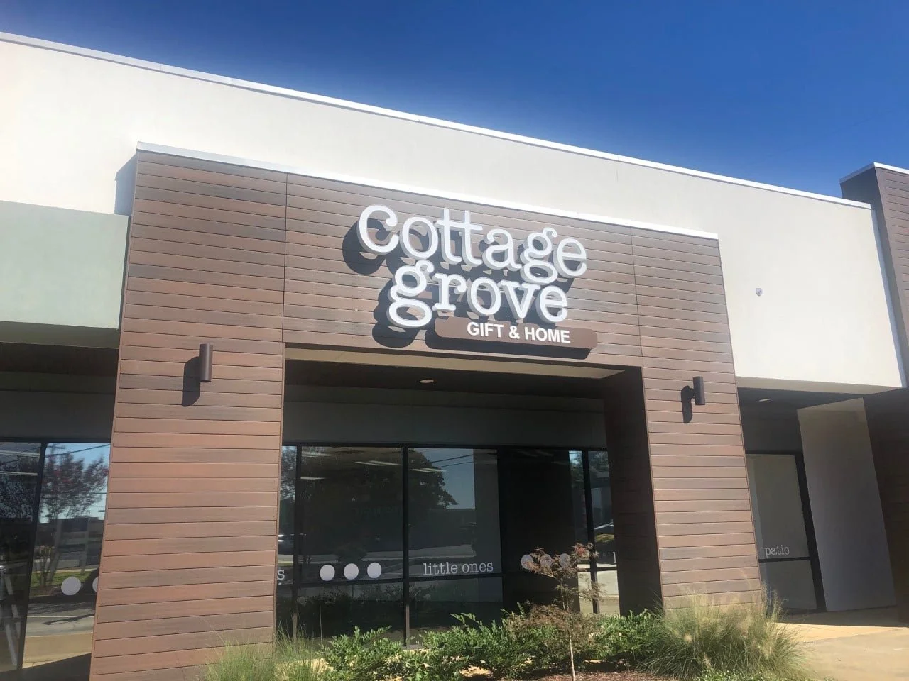 Exterior of Cottage Grove Gift & Home store with a modern design, brown and white siding, and large glass windows, under a clear blue sky.