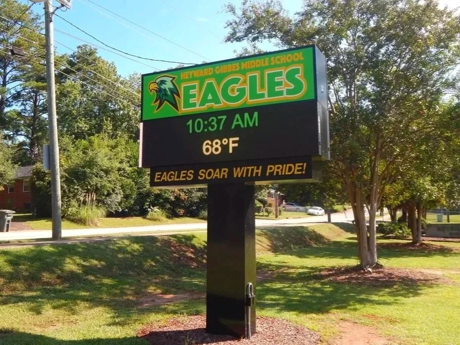 Digital school sign for Heyward Gibbs Middle School featuring a green and yellow eagle logo, displaying the time as 10:37 AM, the temperature at 68°F, and a message reading "Eagles soar with pride!"