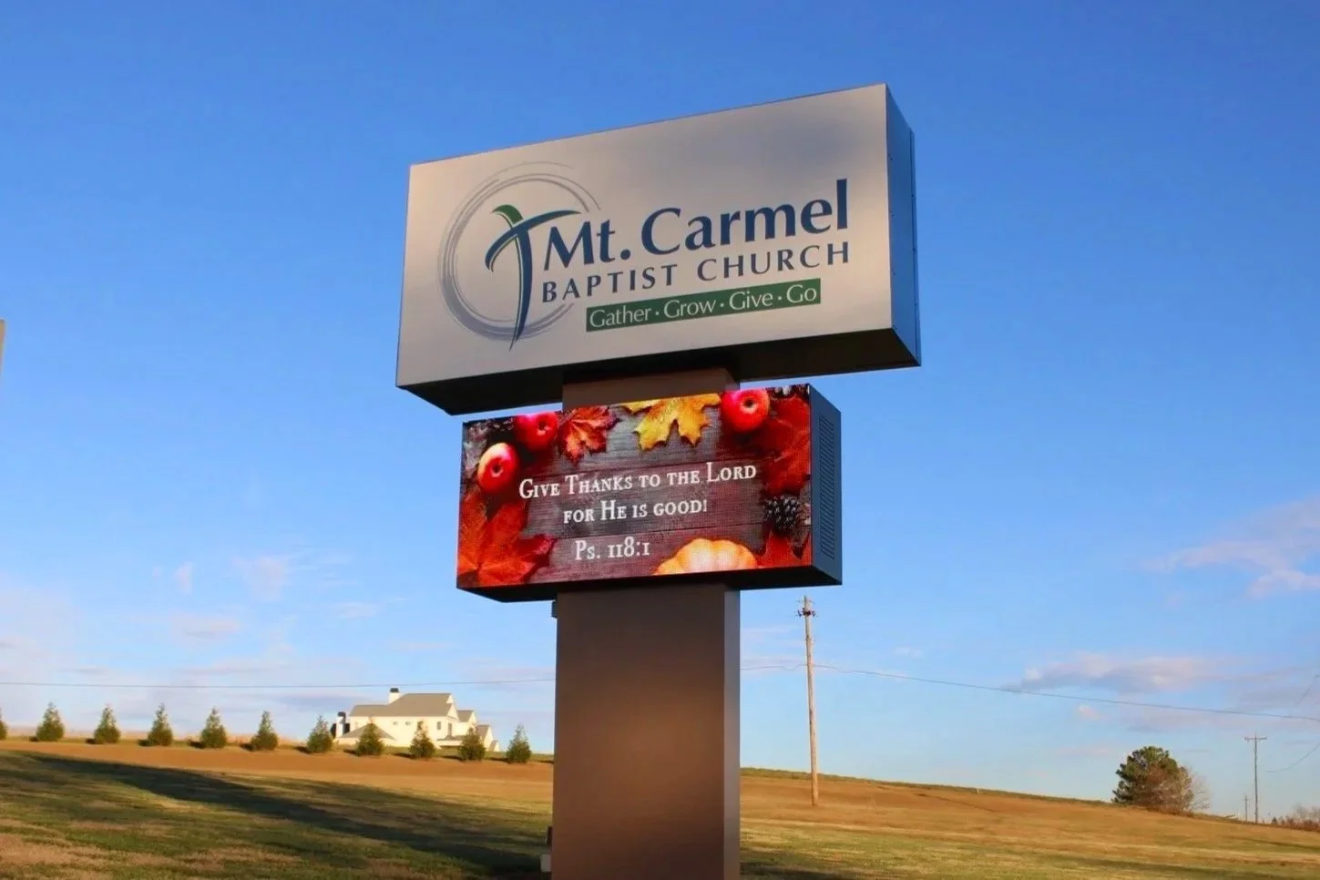 A billboard outside Mt. Carmel Baptist Church with a religious message. The upper part displays the church's name, logo, and slogan: "Gather. Grow. Give. Go." The lower part shows an autumn-themed background with leaves and berries and a verse from t