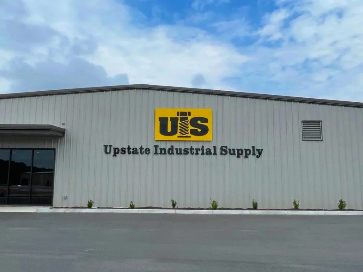 Front of a large industrial building with a sign that reads 'U S' and 'Upstate Industrial Supply' underneath.