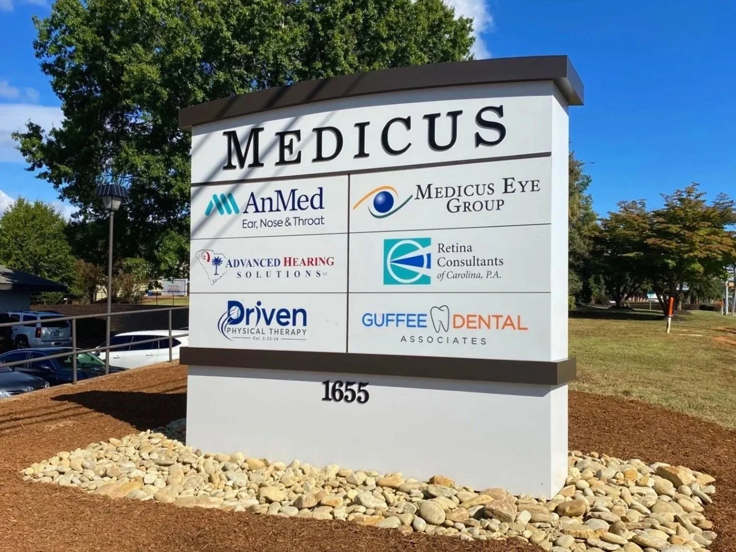 A sign for Medicus, a medical building, displaying logos and names of several health-related businesses including AnMed Ear, Nose & Throat, Medicus Eye Group, Advanced Hearing Solutions, Retina Consultants of Carolina, P.A., Driven Physical Therapy, 