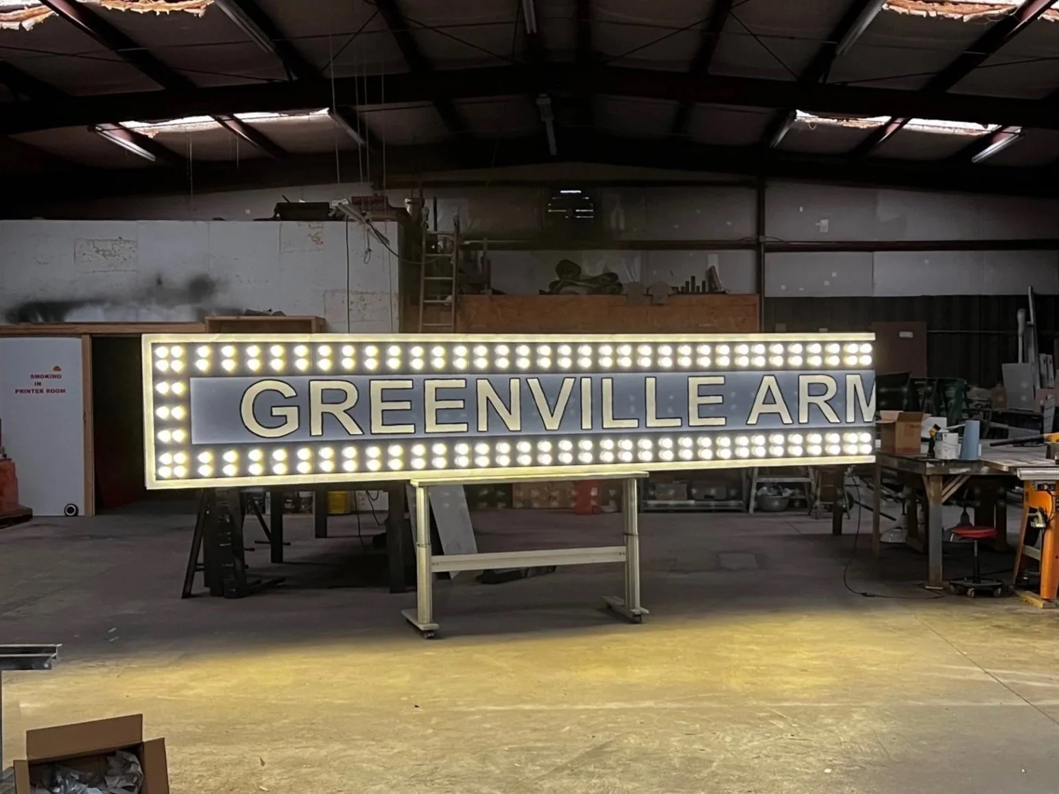 Illuminated sign reading 'GREENVILLE ARM' in a workshop or warehouse setting.