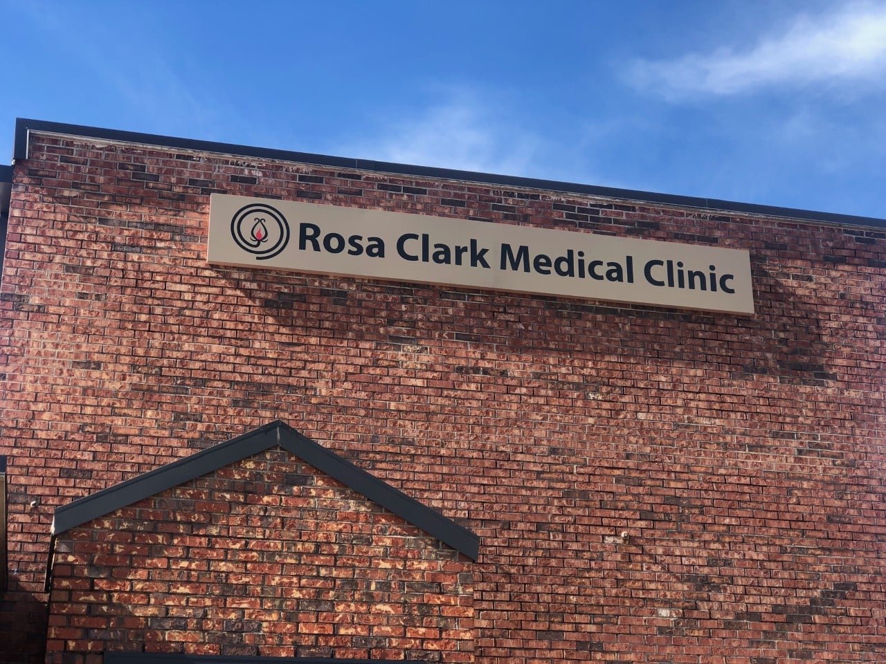 Sign on brick building reads Rosa Clark Medical Clinic with a logo featuring a candle inside a circle.