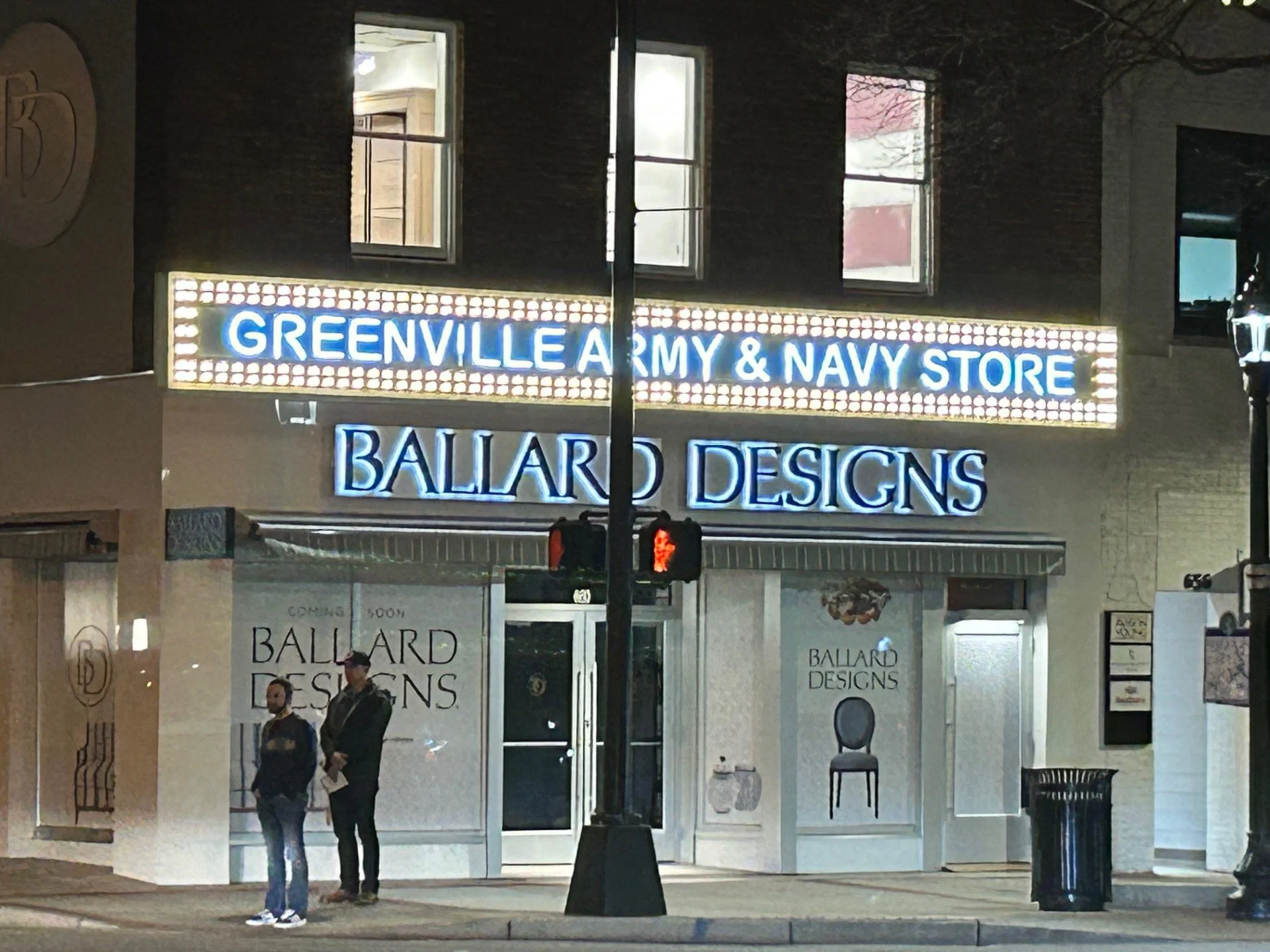 Nighttime storefront of Greenville Army & Navy Store with illuminated sign, and two people standing outside near the entrance.