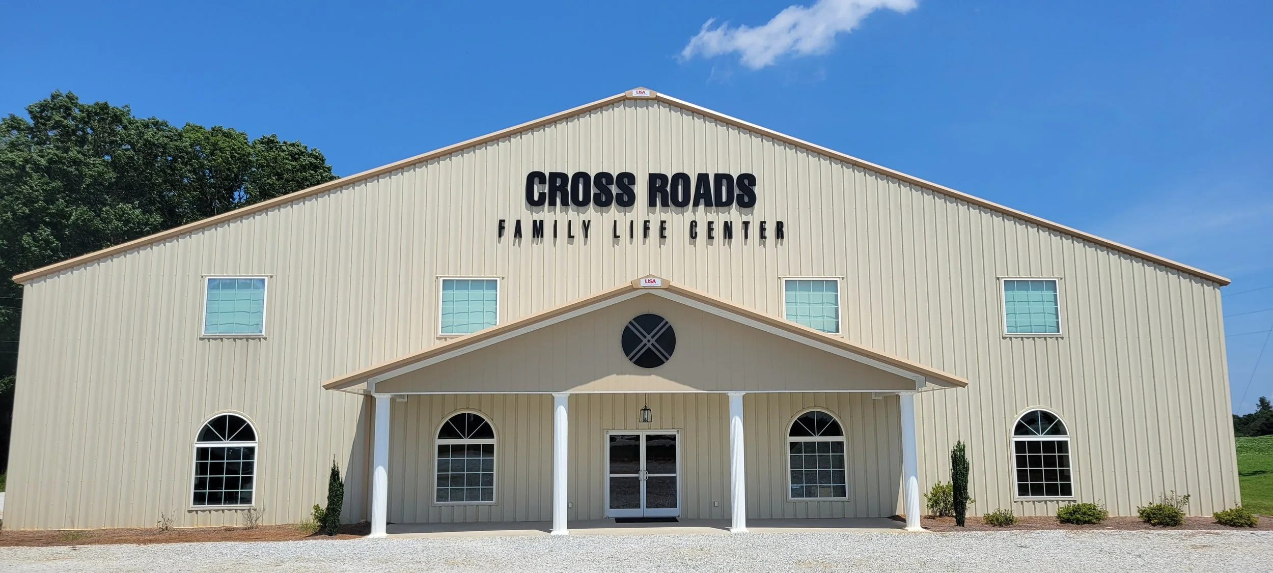 Exterior of a beige building labeled 'Cross Roads Family Life Center' with a blue sky background.
